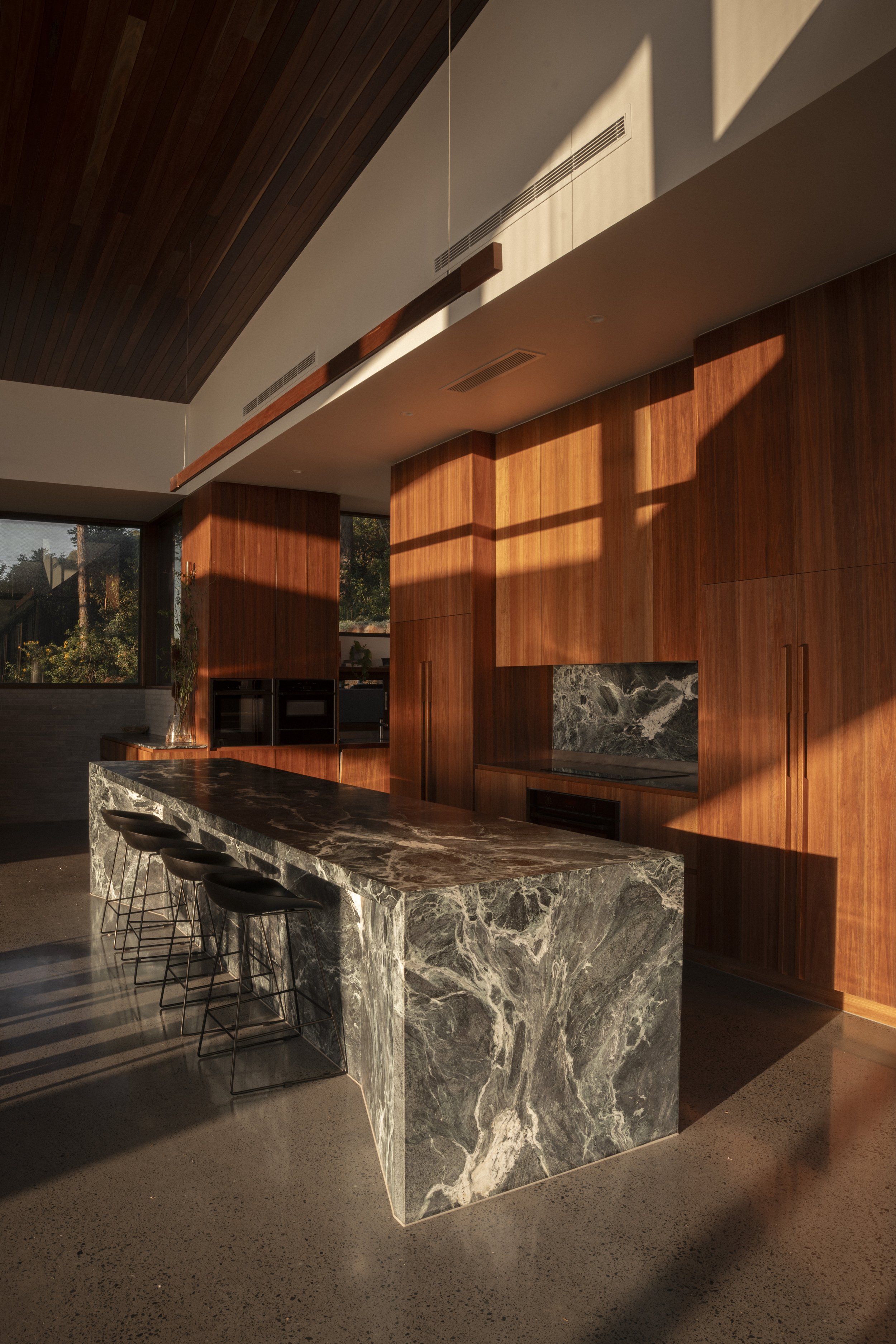 Modern kitchen with a marble island, wooden cabinets, and black barstools