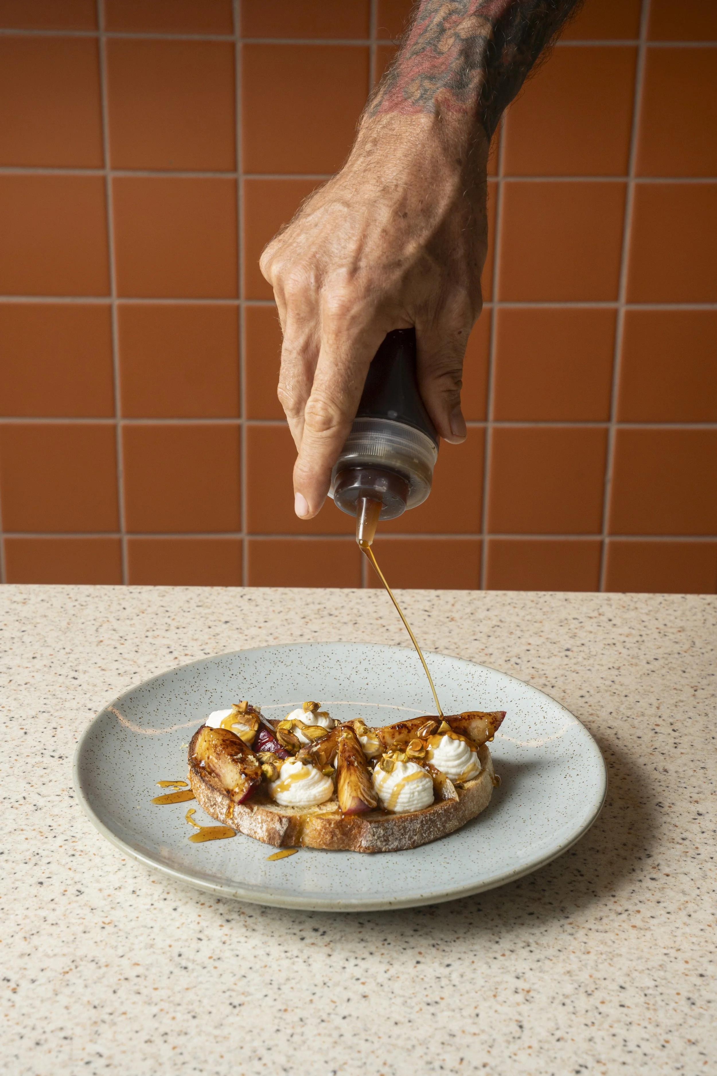 Hand drizzling honey over toast with whipped cream and figs on a plate. Gold Coast | Byron Bay Food Photography by Joey Bailey