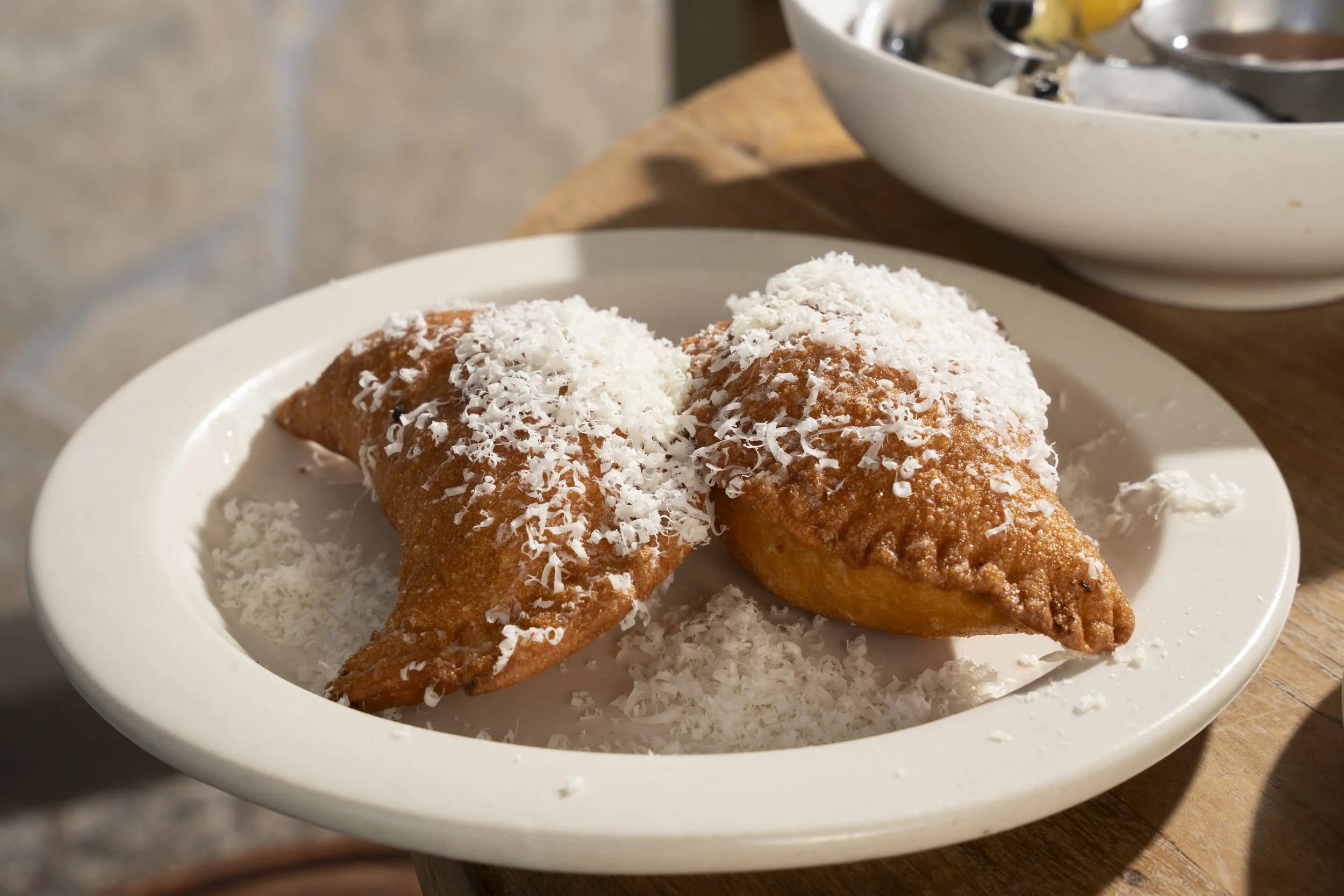 Two fried empanadas topped with shredded cheese on a white plate. Gold Coast Food Photography by Joey Bailey
