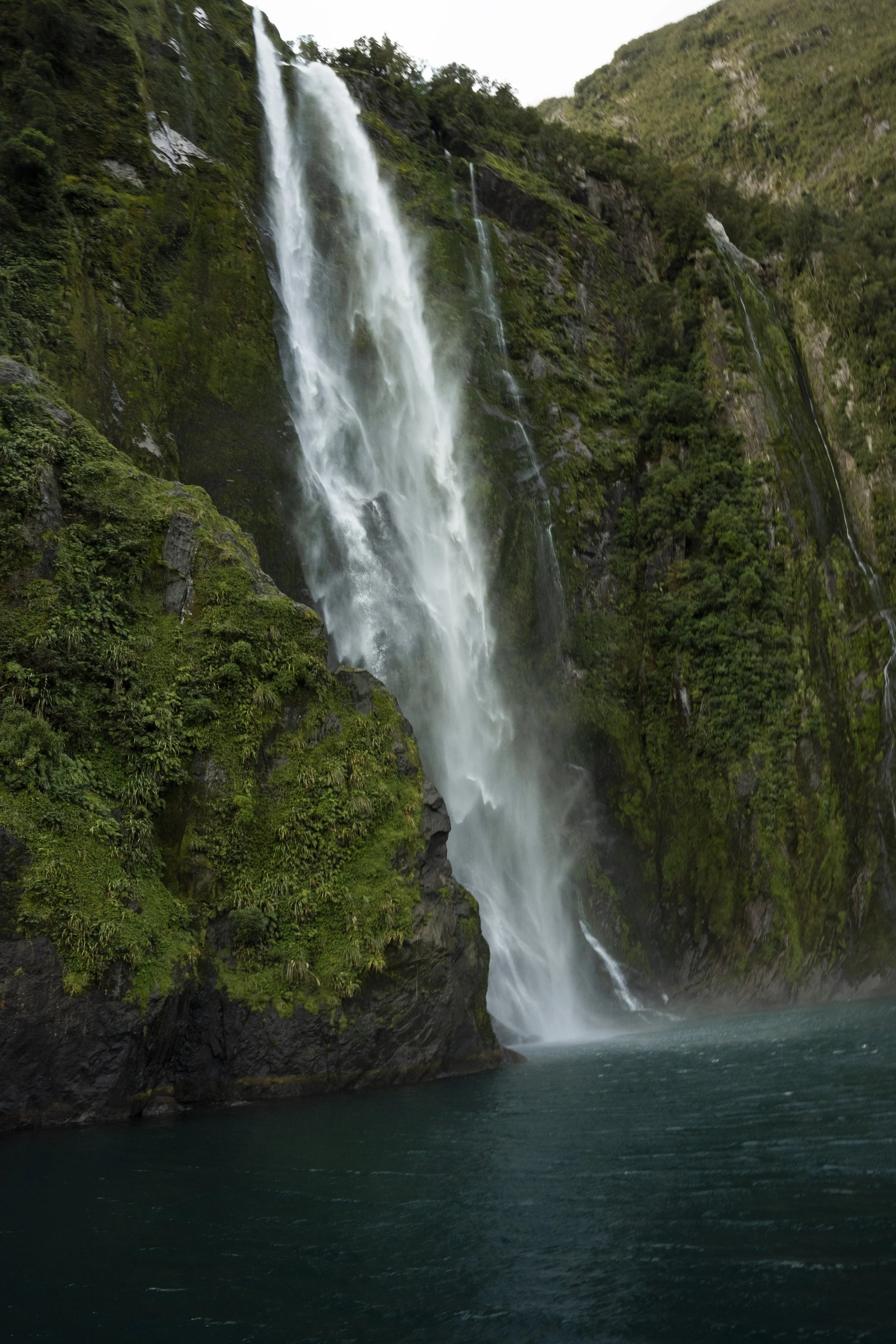 Waterfall cascading down a lush, green cliff into a body of water.