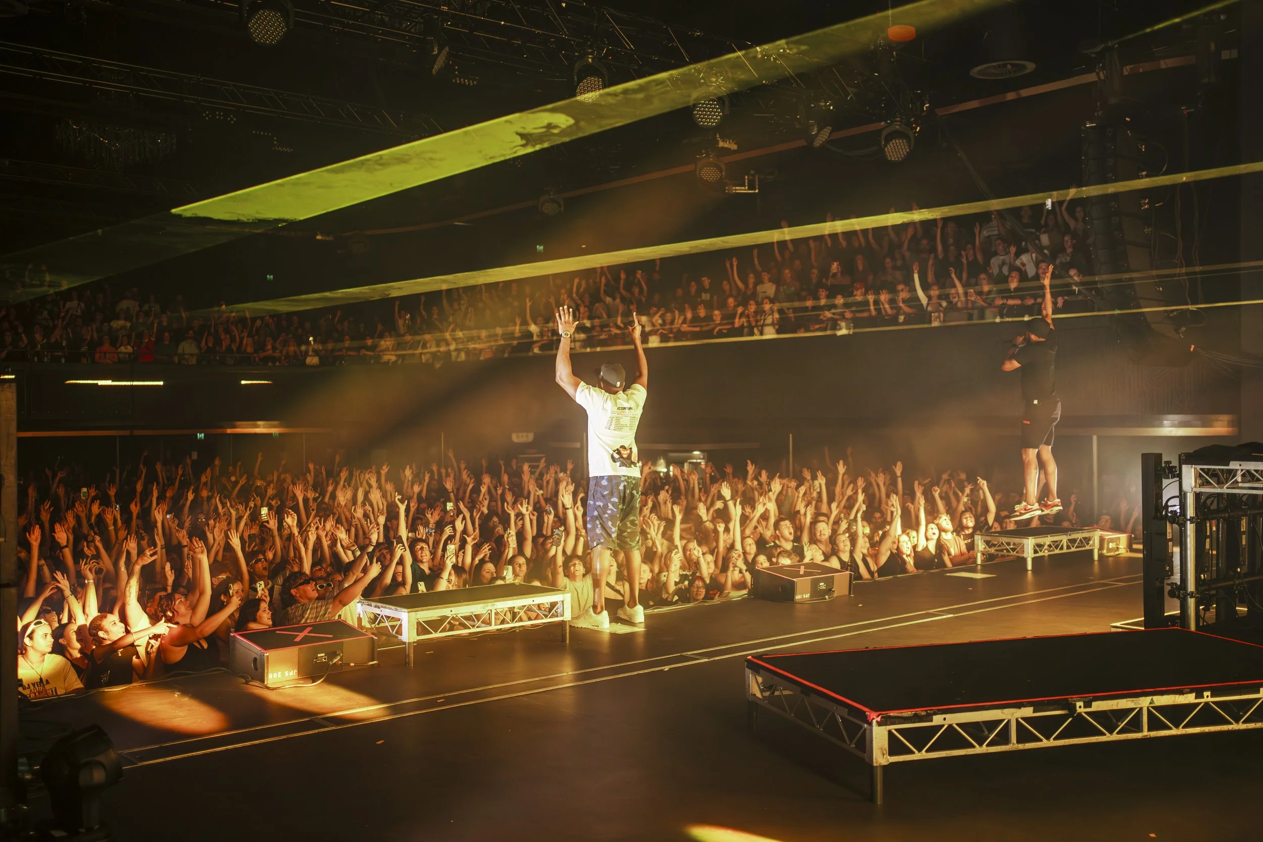 Dizzie Rascal performers on stage at a concert with a large, enthusiastic crowd raising their hands.