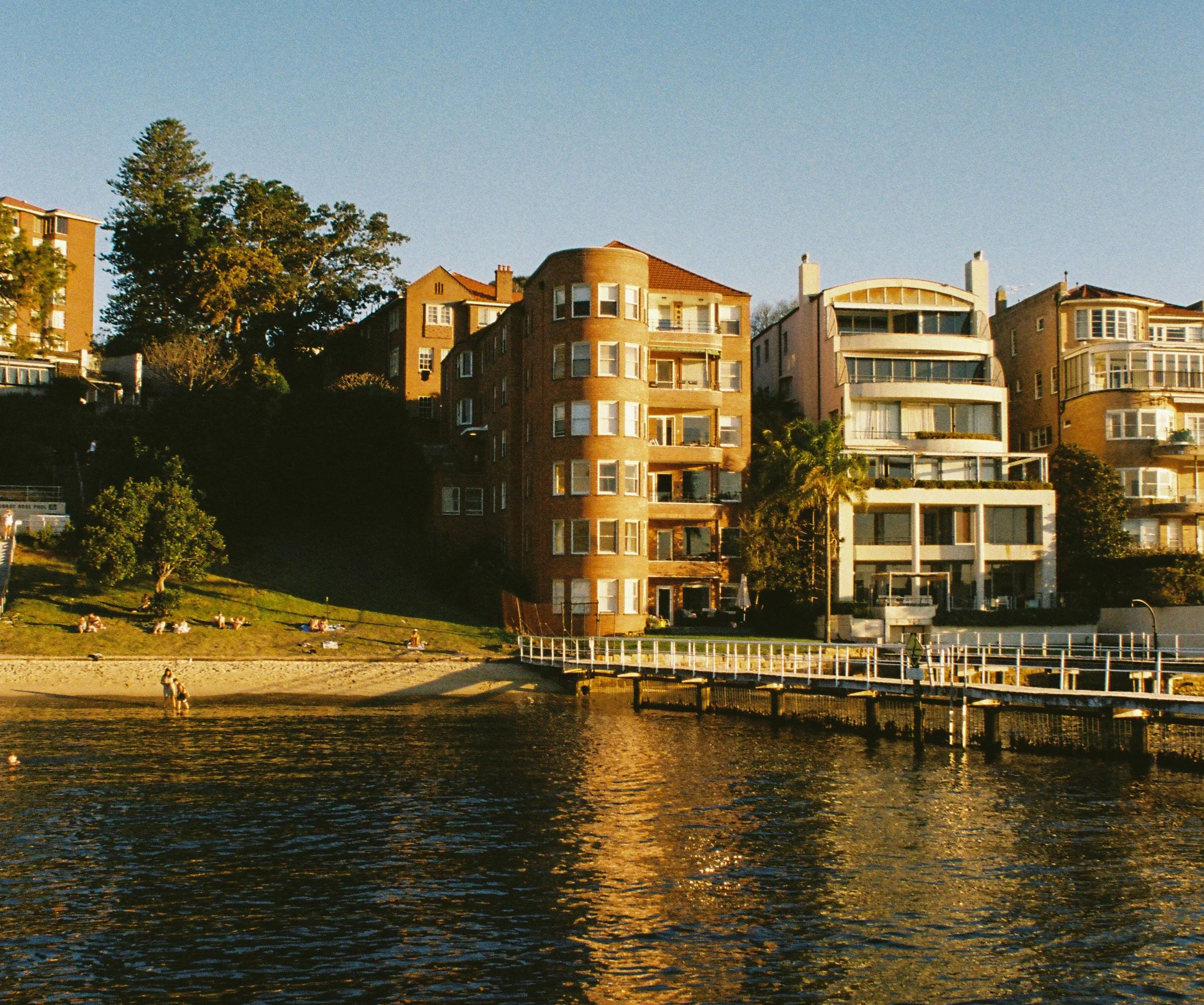 A row of multi-story houses with various architectural styles along a hillside, view from a body of water at sunset. Garron Tower Art Deco architecture