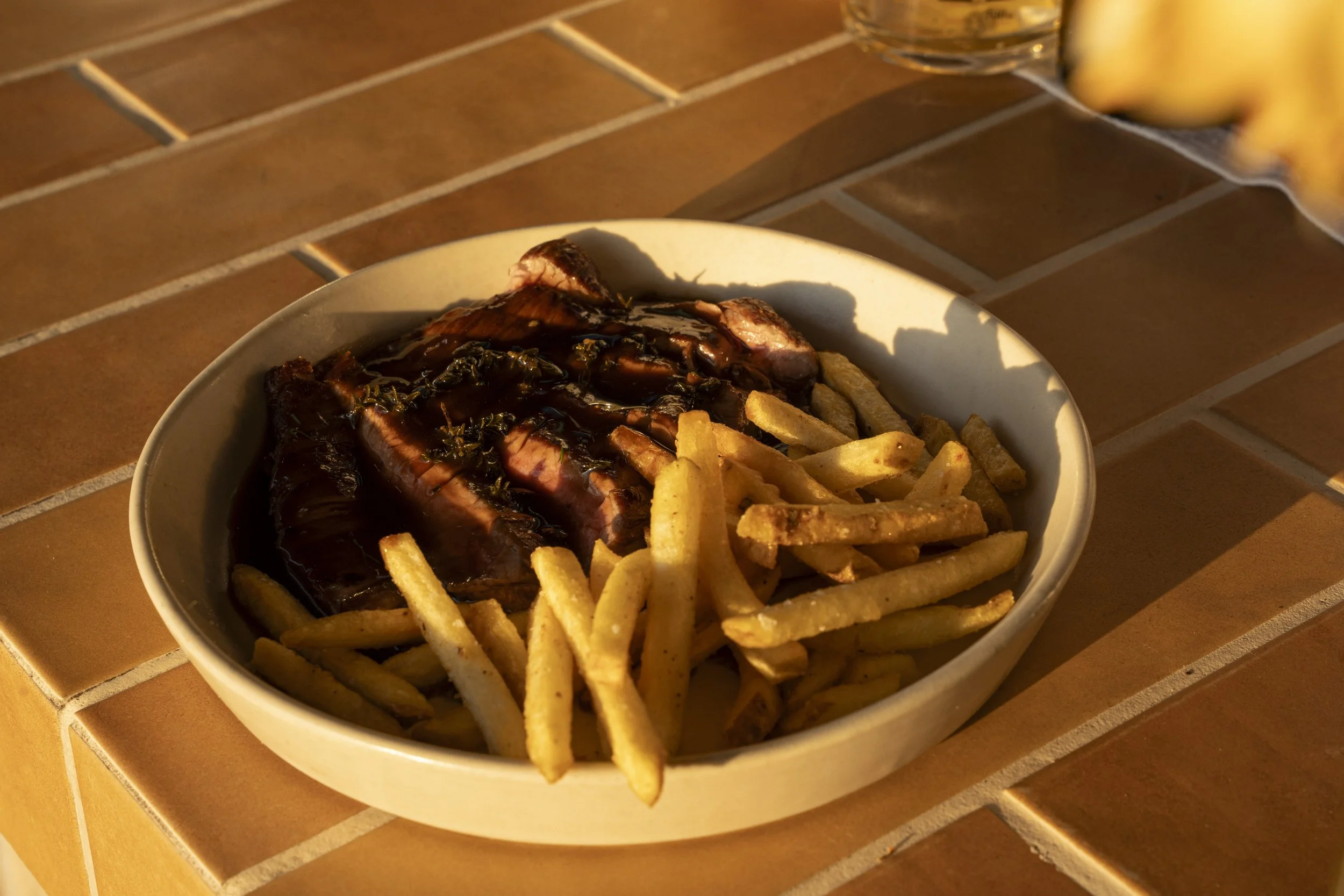 Bowl of French fries and sliced steak topped with dark gravy on a tiled surface. Gold Coast Food Photography by Joey Bailey
