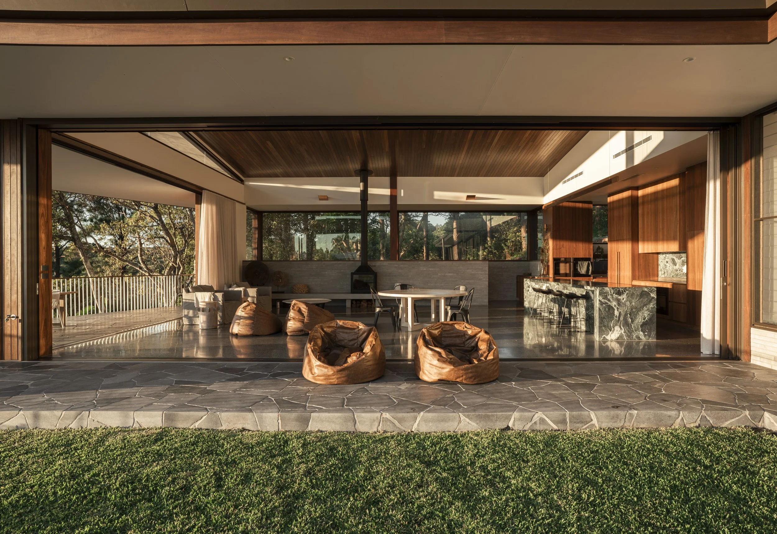 Open living space with large glass doors, outdoor terrace, bean bags, and a kitchen with wooden cabinets.Gold Coast | Byron Bay Architectural Photography by Joey Bailey