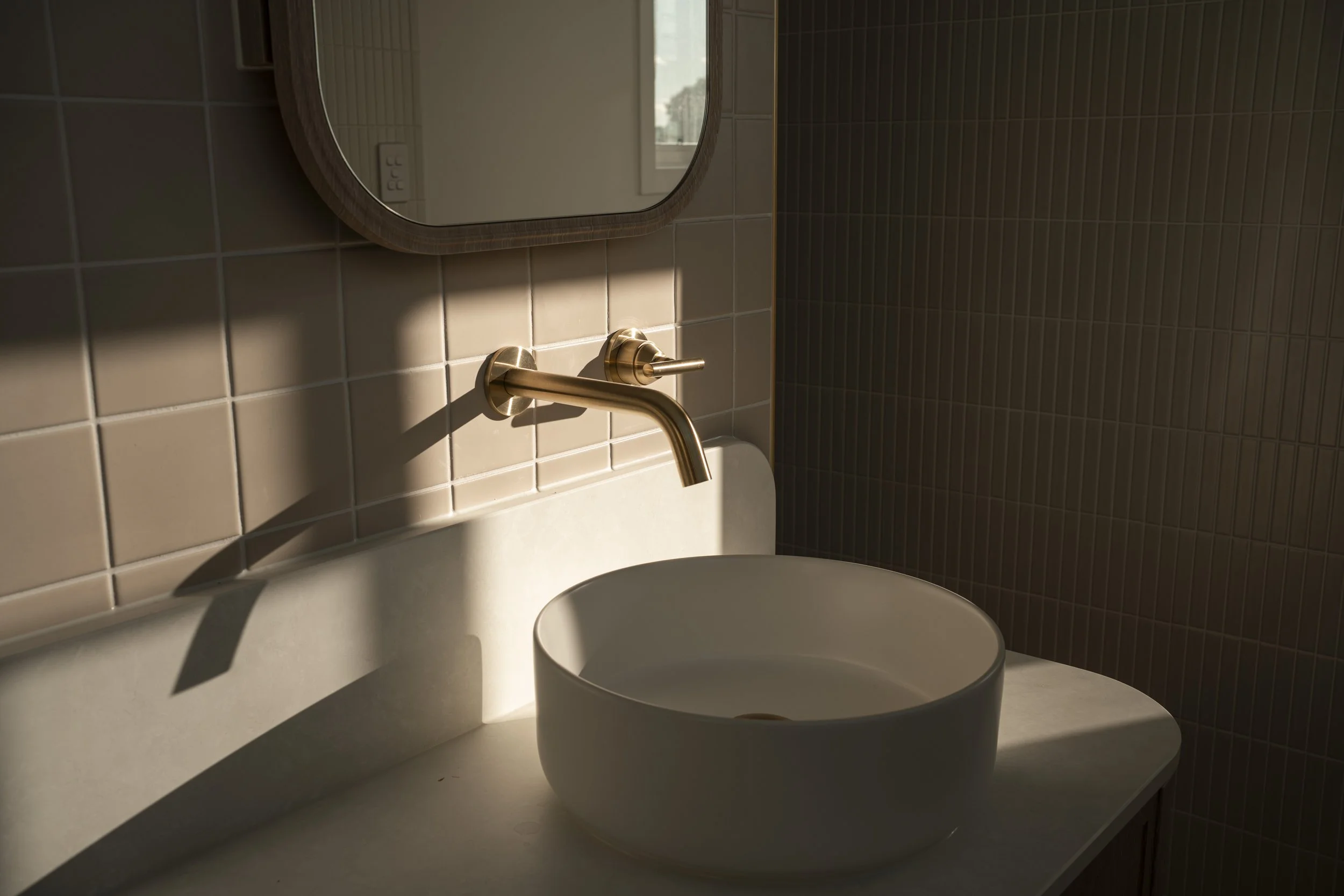 Bathroom sink with a round white vessel and a gold wall-mounted faucet, illuminated by warm sunlight. Architectural photography by Joey Bailey, Gold Coast