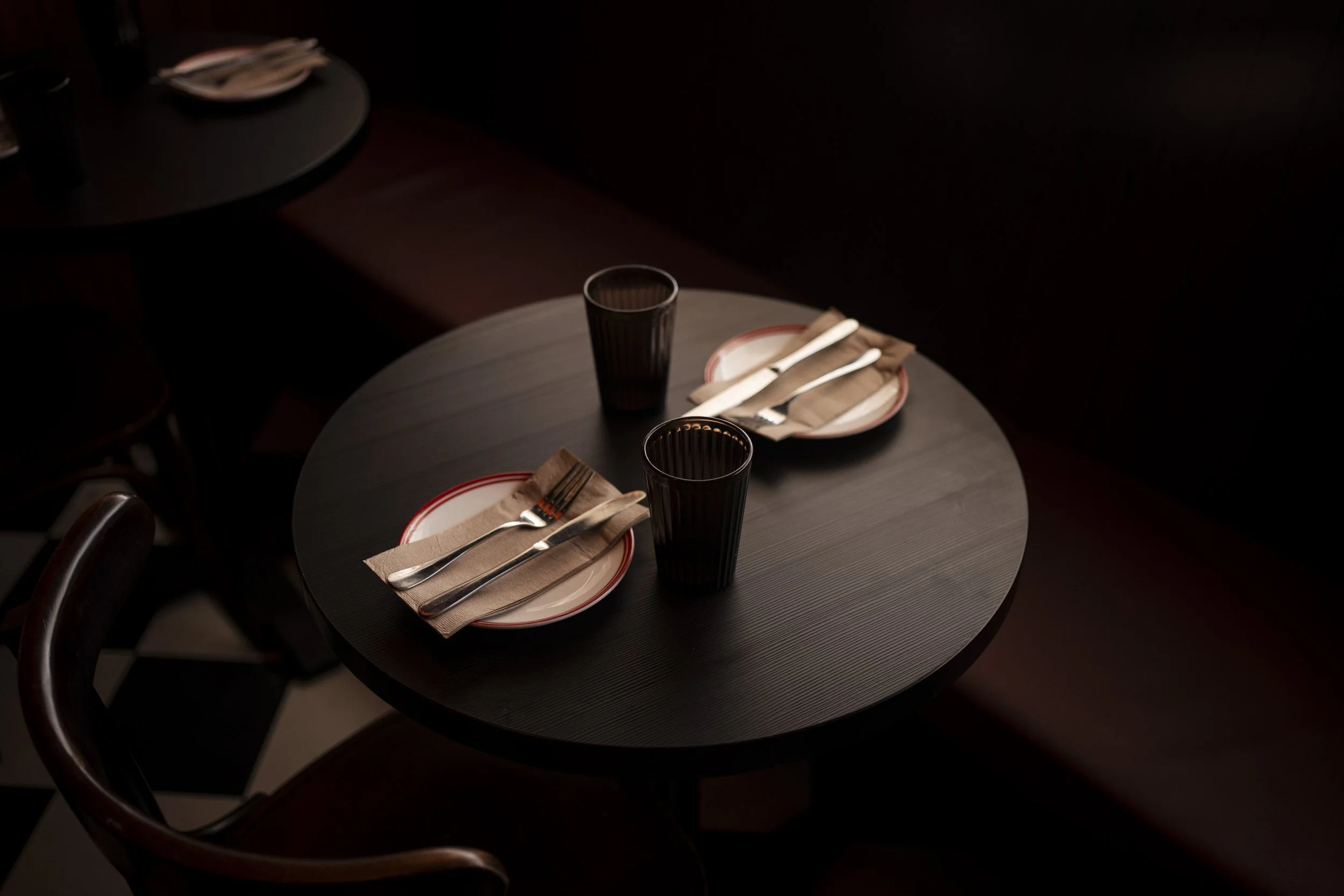 A round, dark wooden table set for two in a dimly lit environment. Gold Coast restaurant food photography 