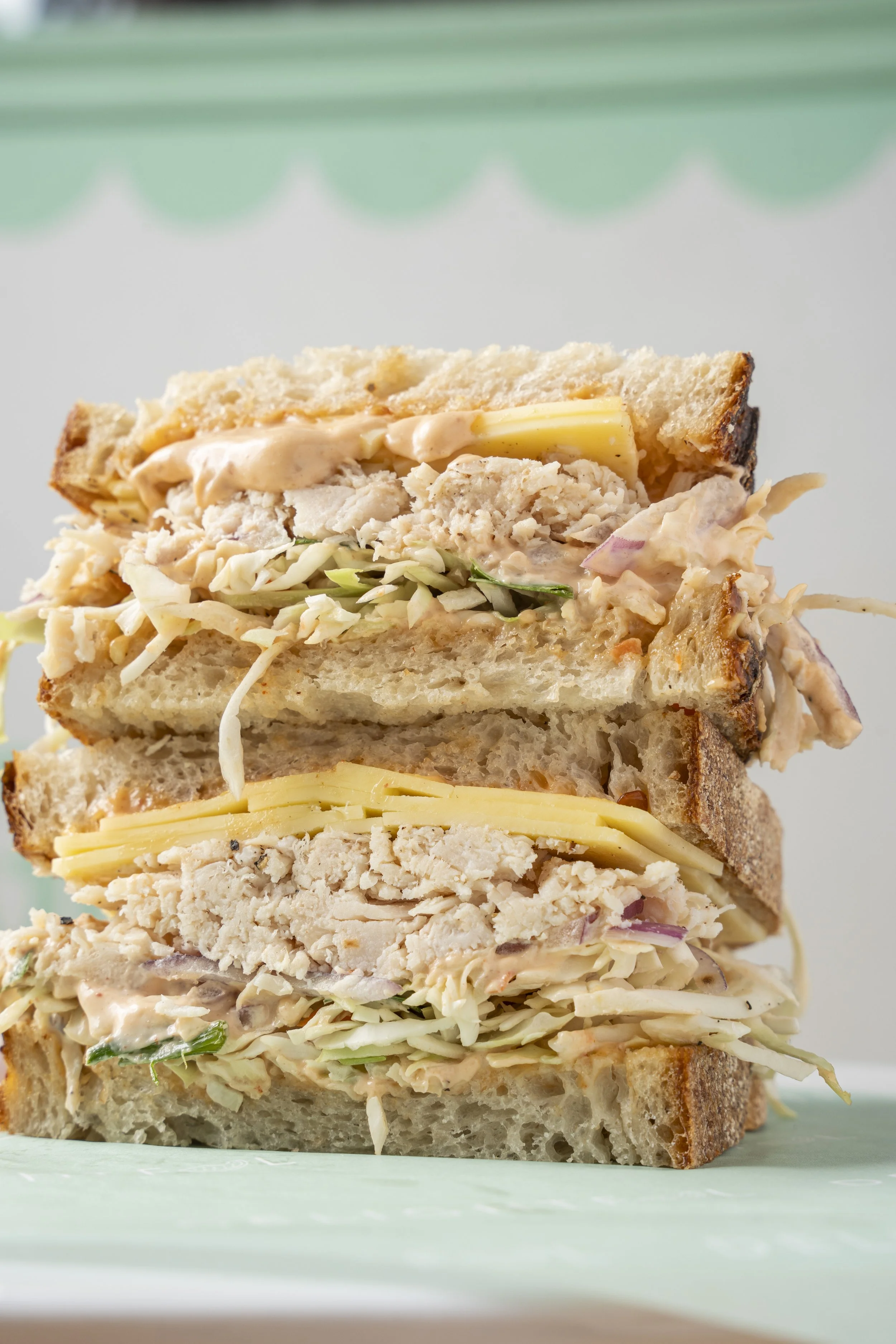 Close-up of a stacked sandwich with layers of shredded chicken, cheese, coleslaw, and creamy dressing on toasted bread. Gold coast food photography by Joey Bailey