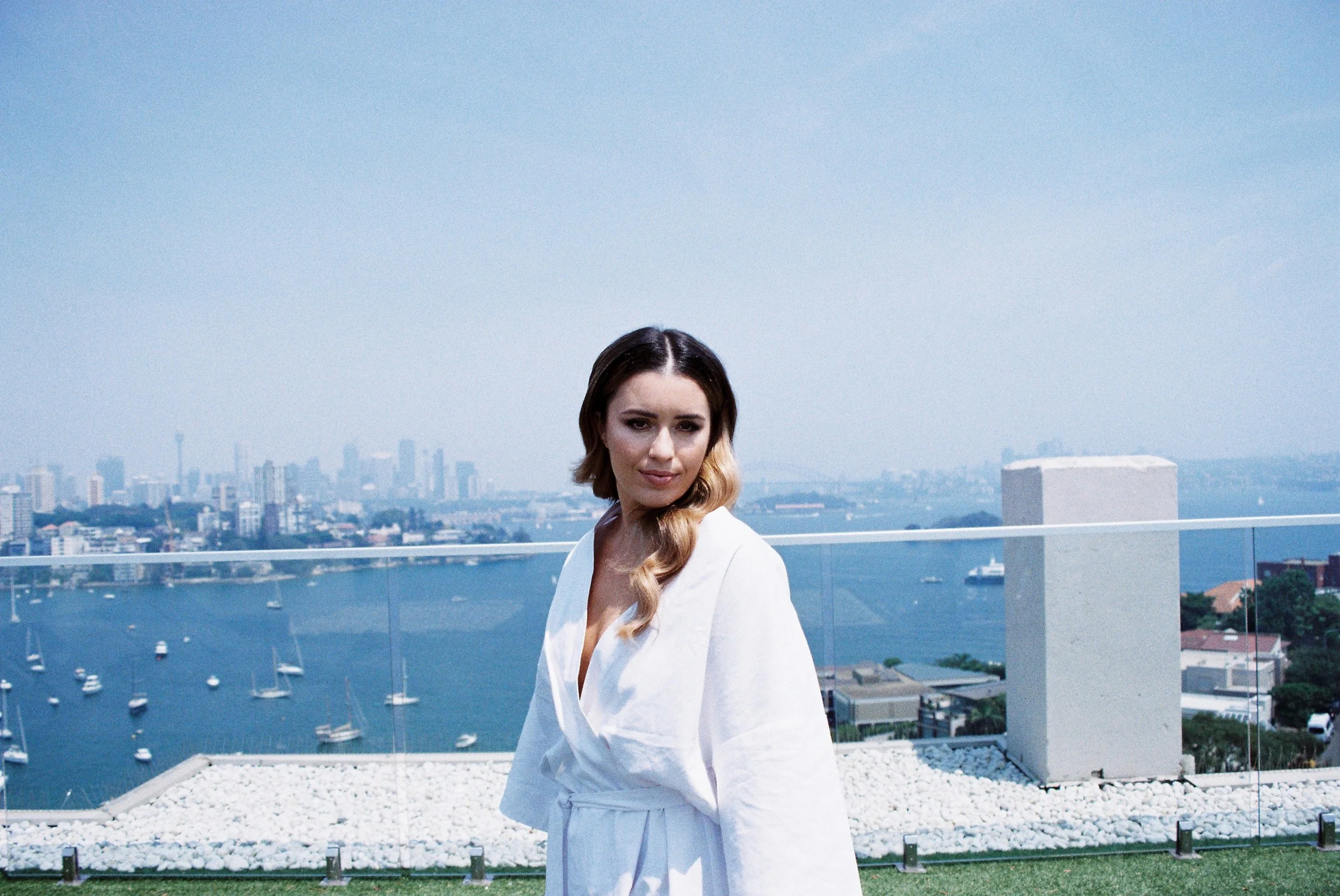 Woman in white robe on balcony with city skyline and bay view