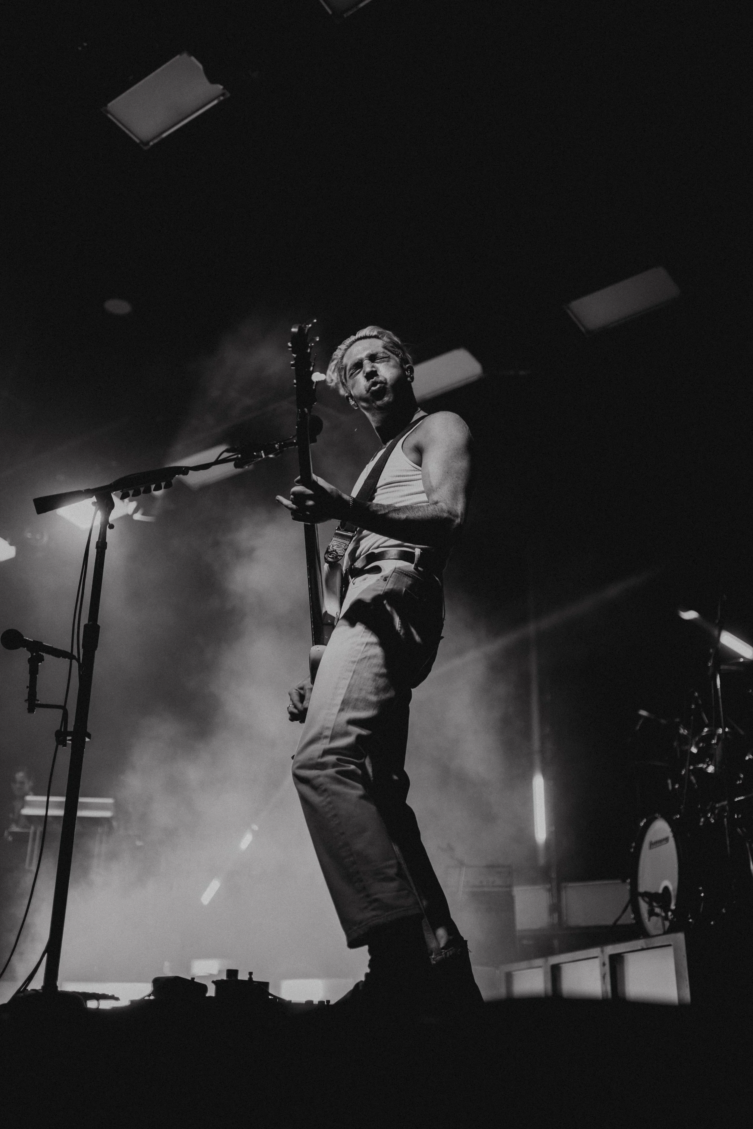 Black and white photo of a musician playing guitar on stage with dramatic lighting and smoke.