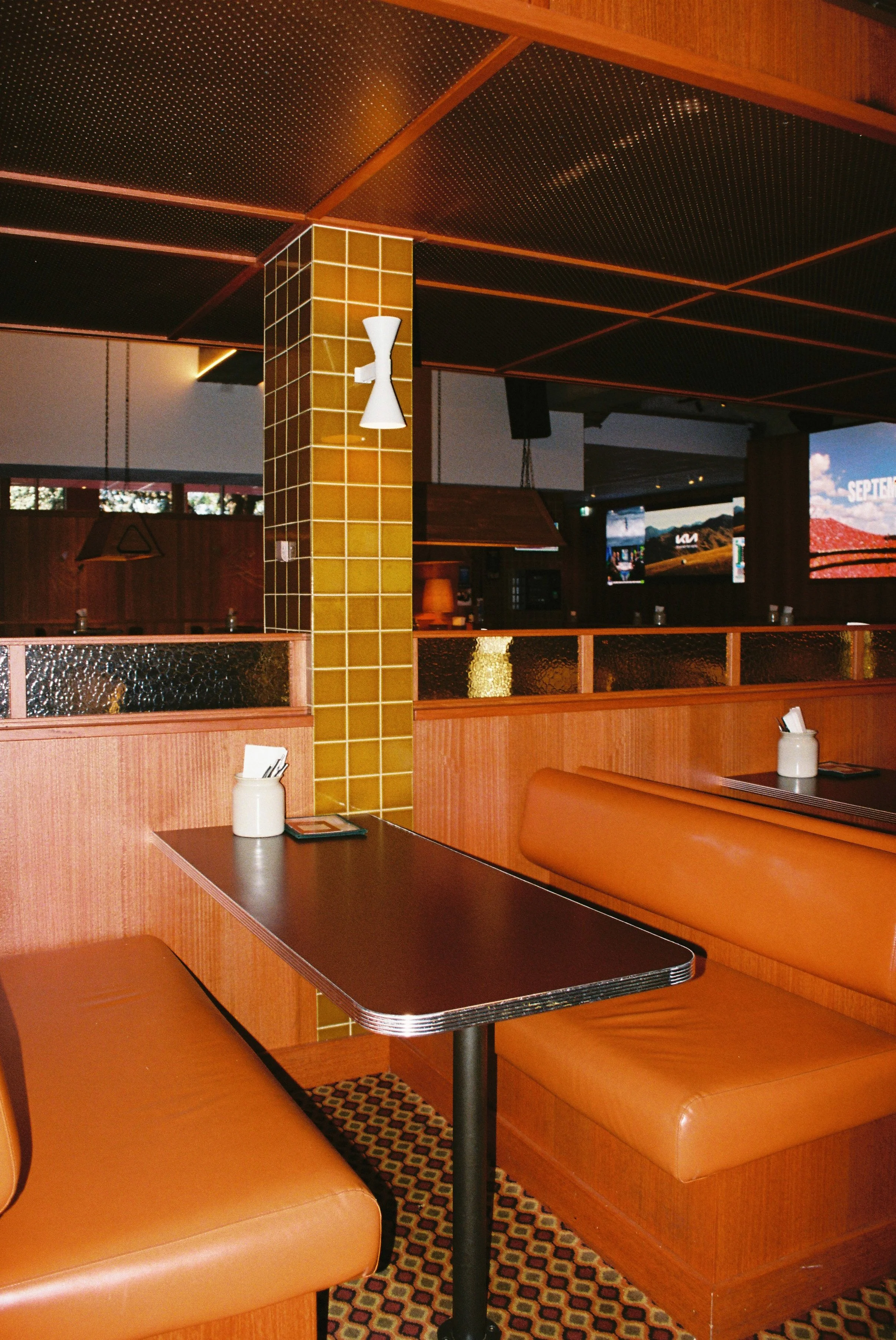 Interior of a retro-style restaurant with orange leather booths, black tables, a yellow tiled column, and a patterned carpet. Sydney interior photography