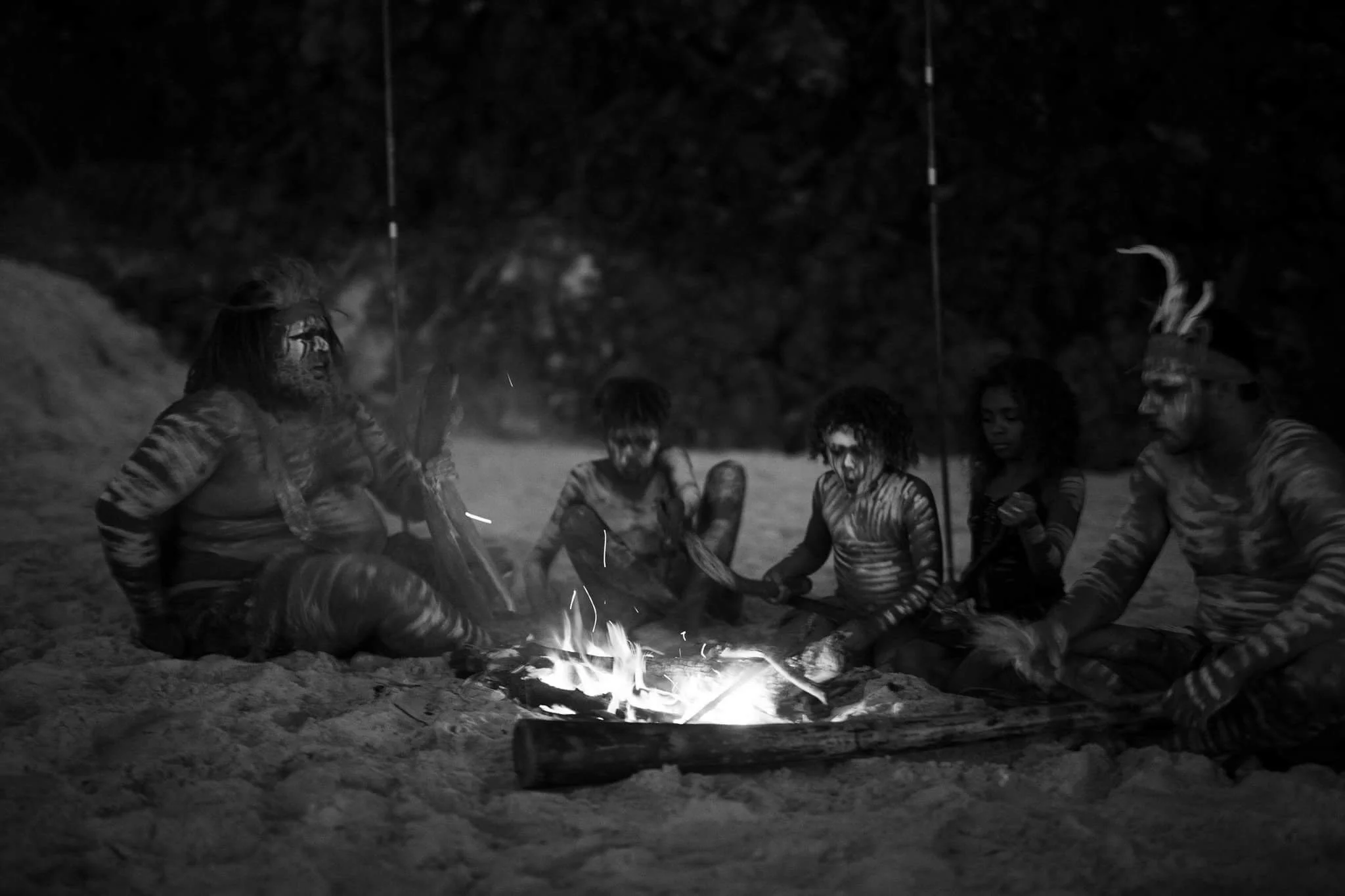 A group of people with body paint sitting around a campfire at night.