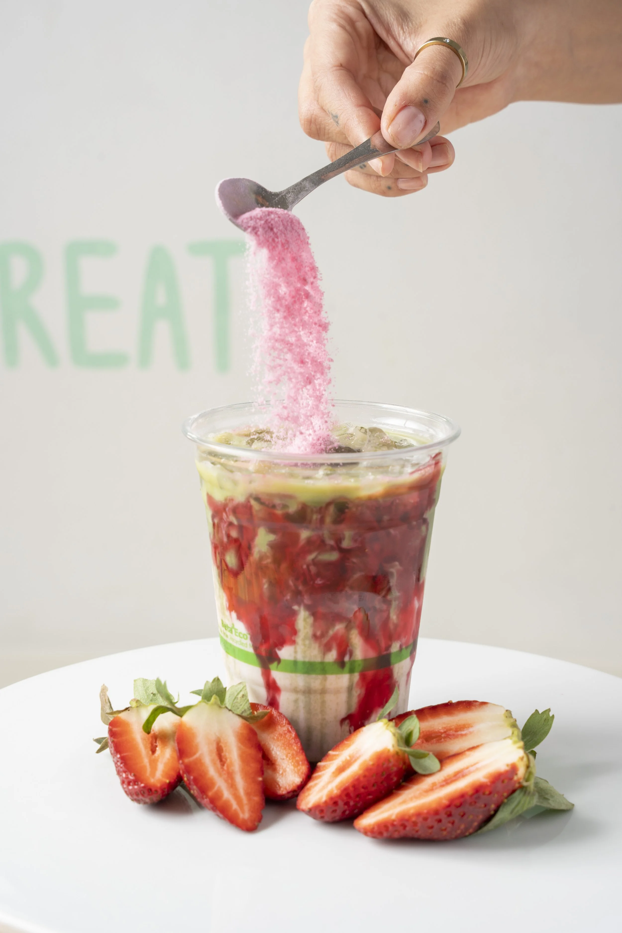 Person pouring pink powder into a strawberry smoothie topped with fresh strawberries on a white plate. Gold Coast Food photography by Joey Bailey