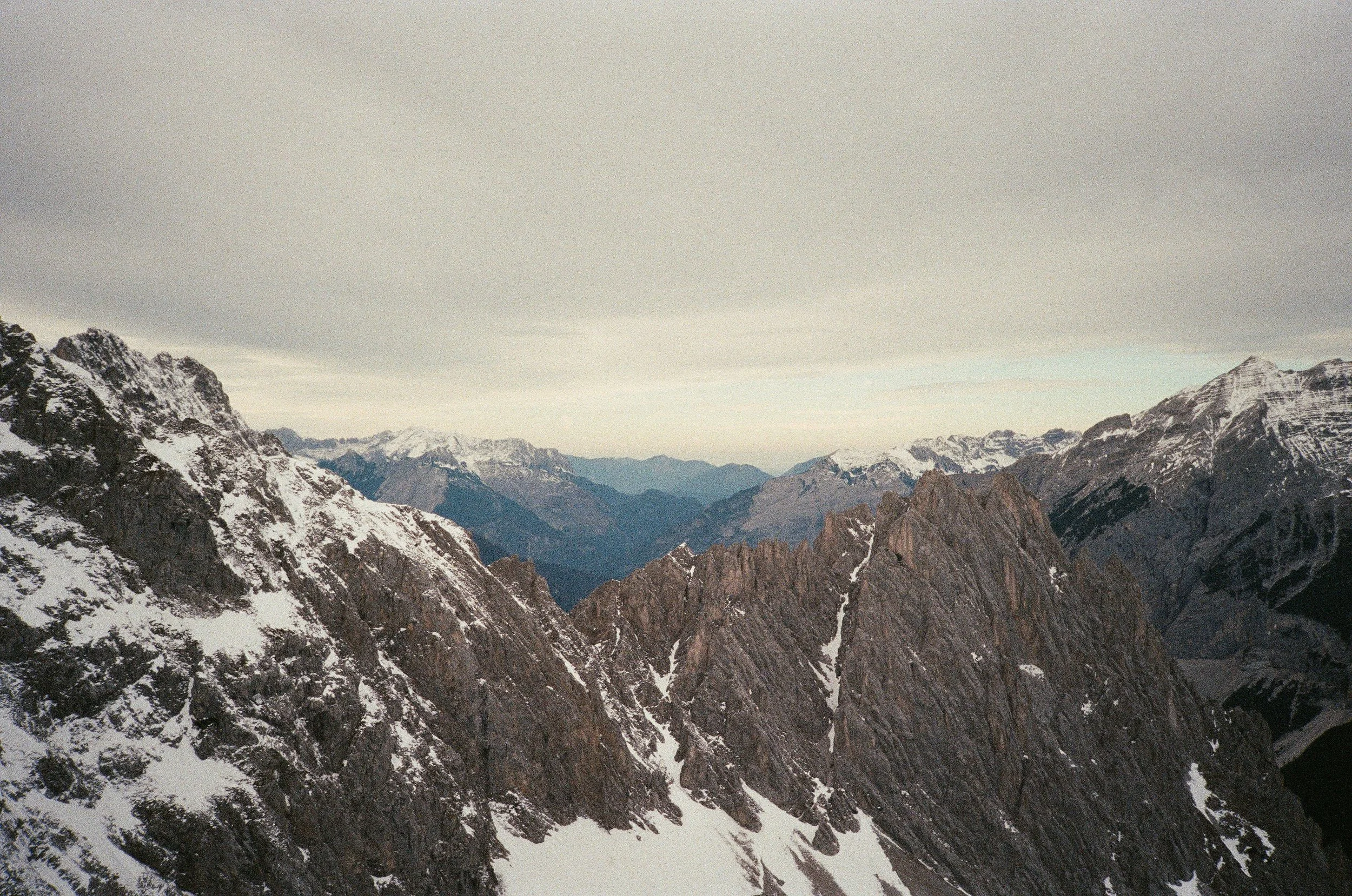 Mountain range with snow-covered peaks under an overcast sky.