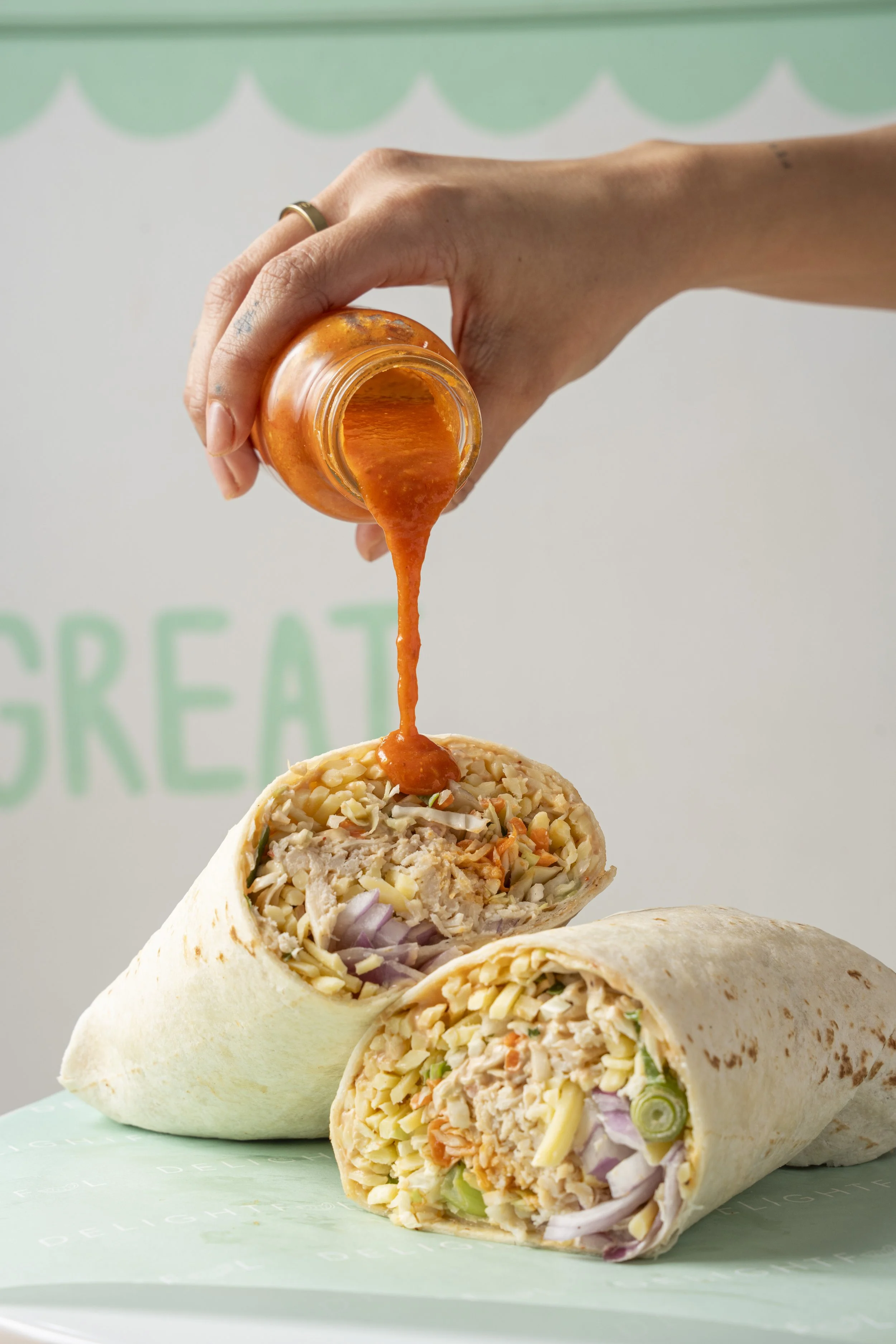A person pouring orange sauce over a chipotle chicken wrap with vegetables. Gold coast food photography by Joey Bailey