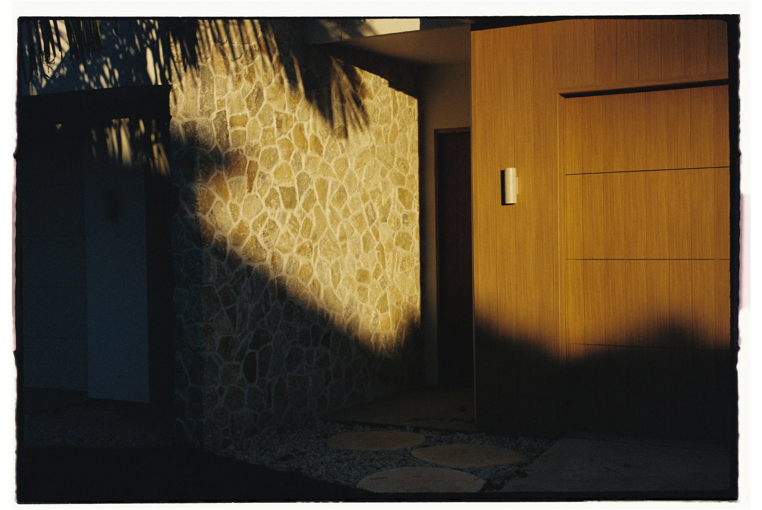 Modern house entrance with stone and wooden wall, shadowed plants, and circular stepping stones. Architecture photography Gold Coast by Joey Bailey
