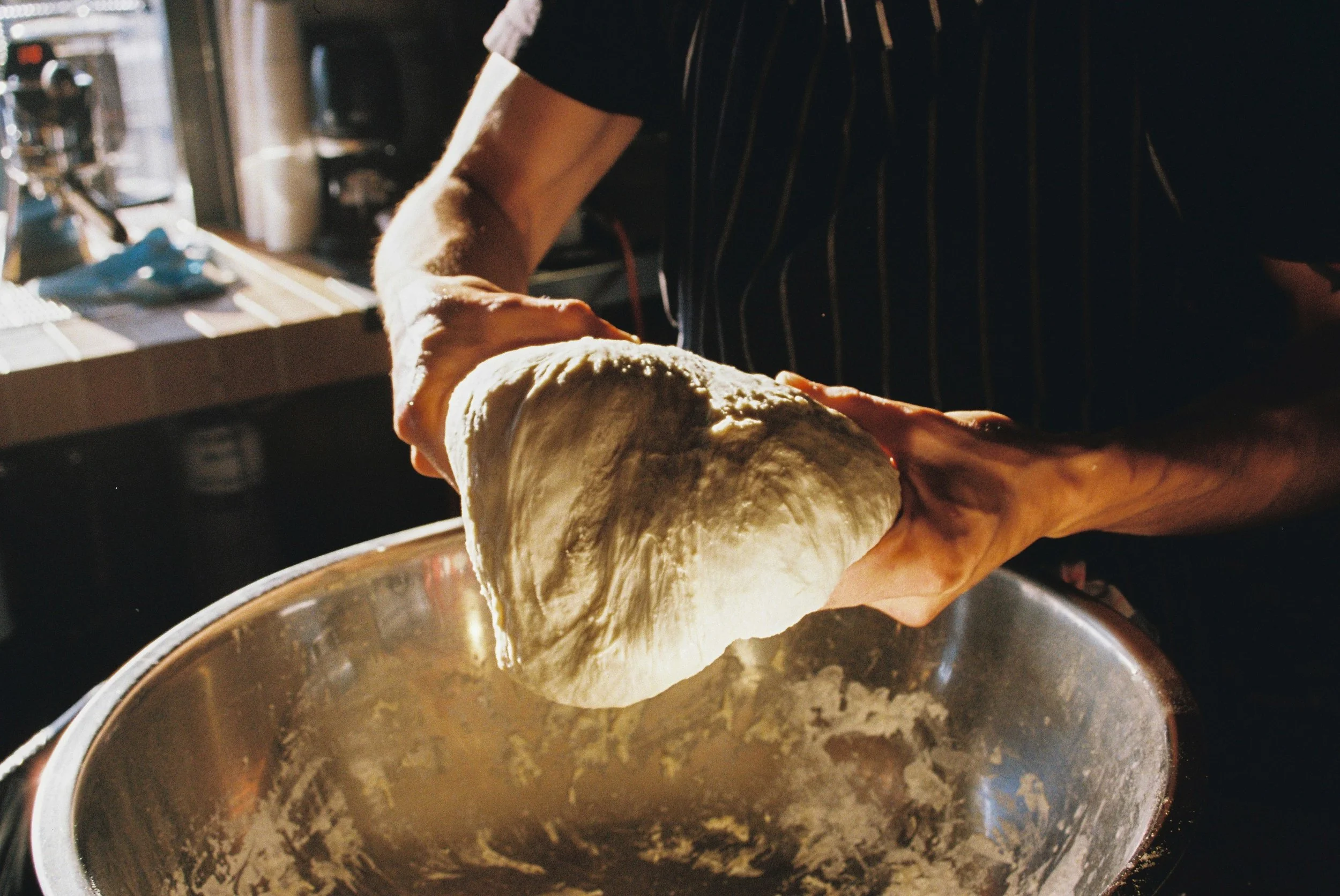 Person kneading pizza dough in a mixing bowl, with sunlight coming through a window.  Gold Coast restaurant marketing 