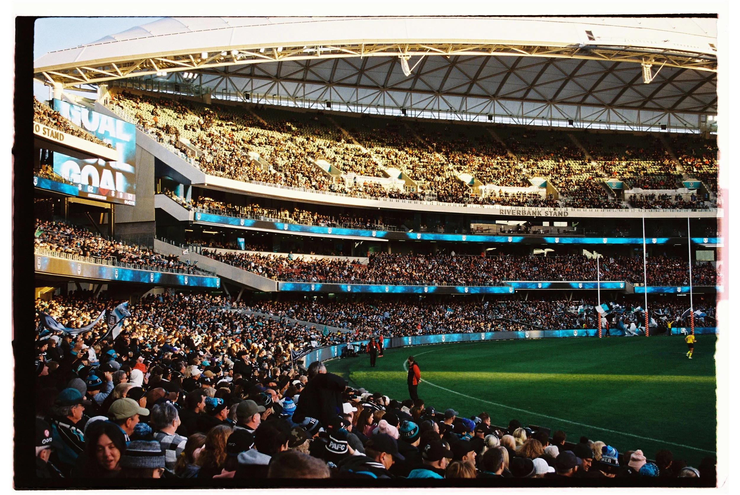 Packed sports stadium during a football game with a large crowd, playing field, and scoreboard visible.