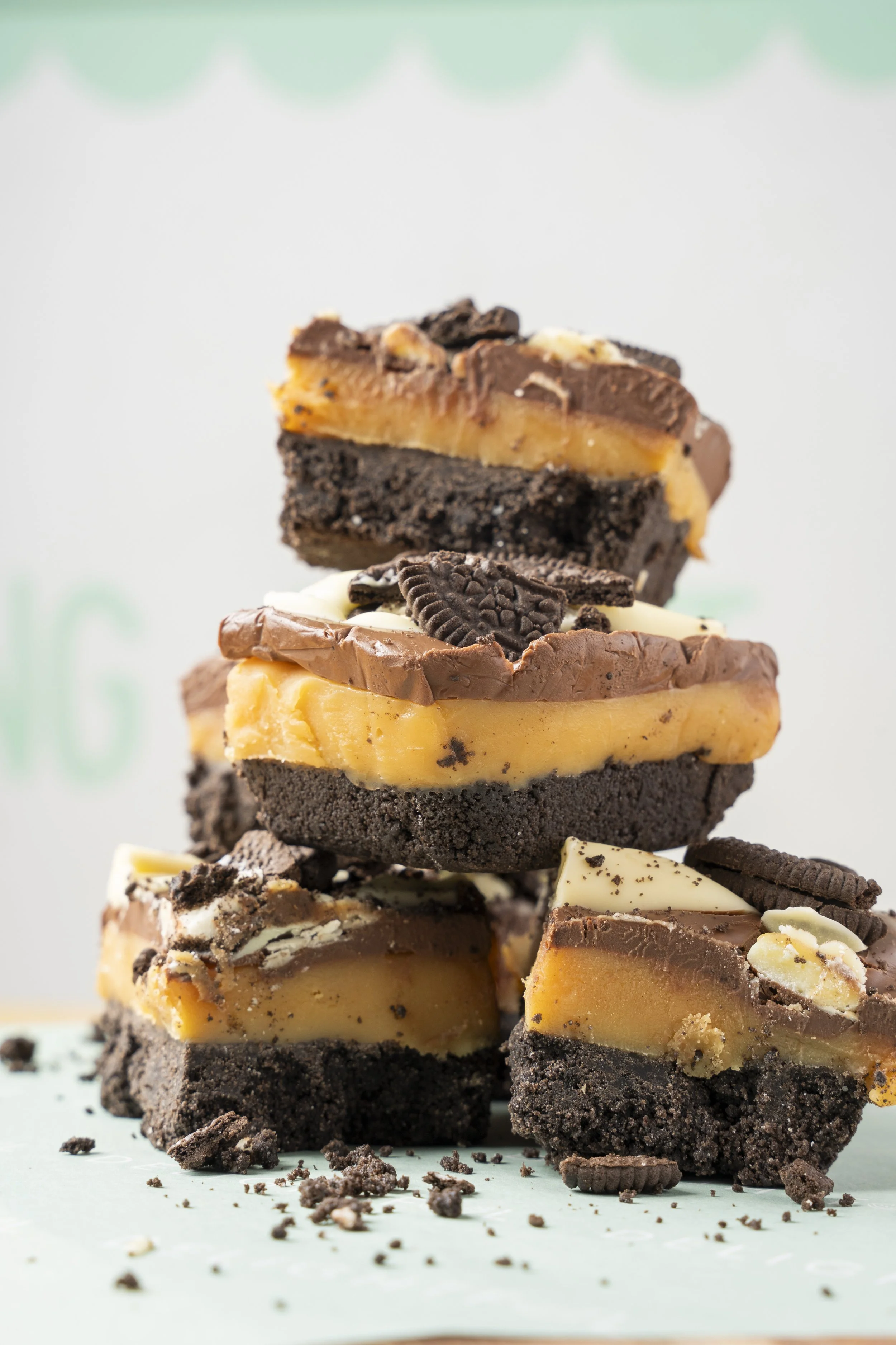 A stack of assorted cookie and brownie bars with chocolate, vanilla, and caramel layers, topped with chopped cookies and broken cookie pieces. Gold coast food photography by Joey Bailey