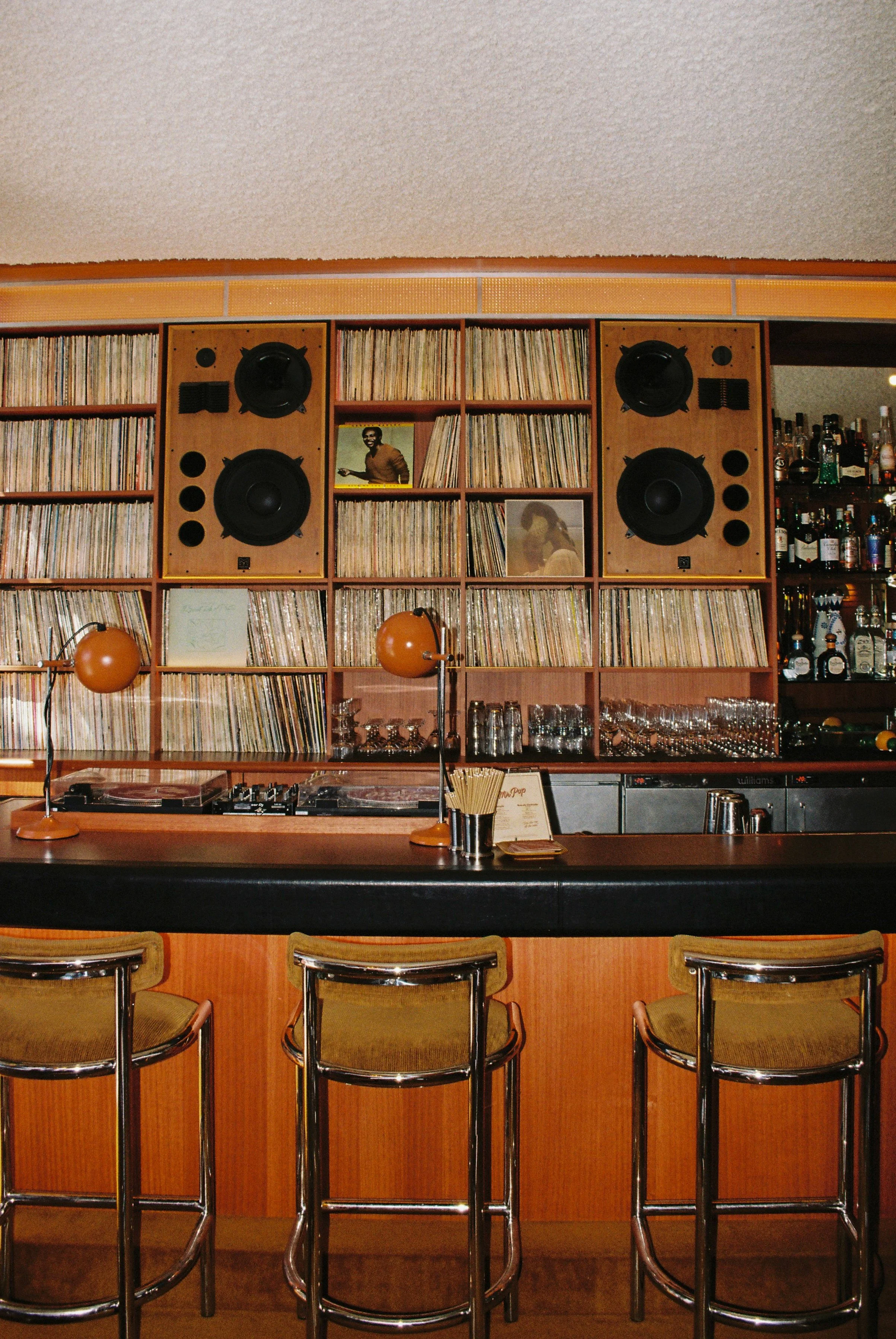 A bar or cafe with a wooden counter and four high chairs, a shelf filled with vinyl records, Sydney interior photography