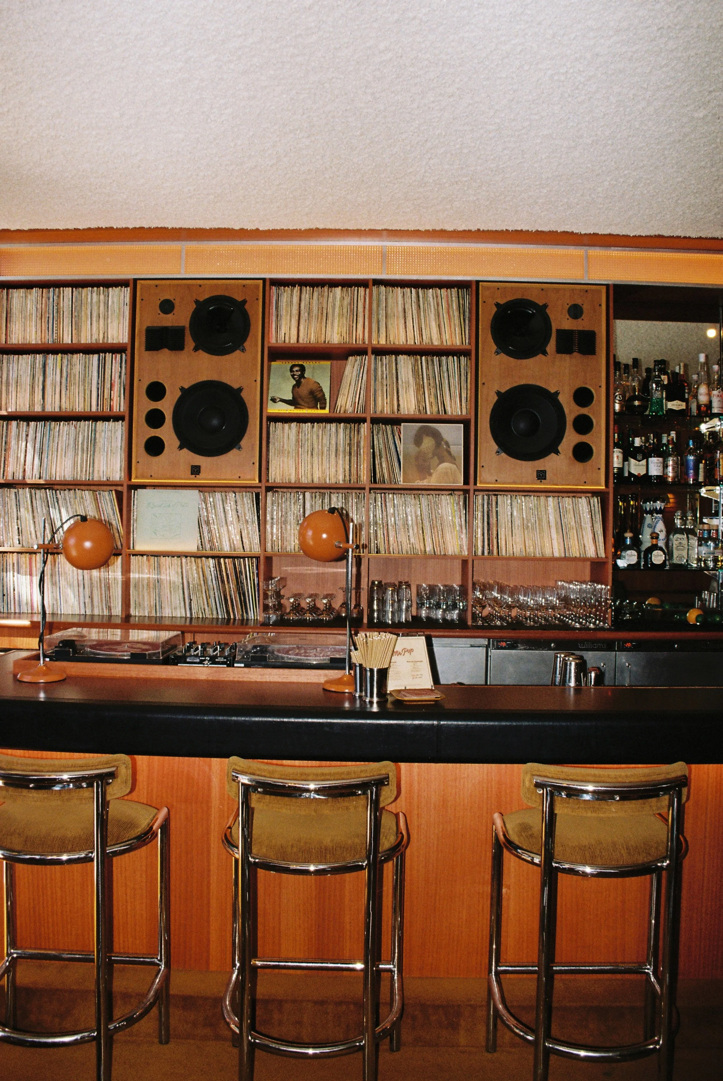 Bar with a vinyl record collection wall, a microphone with a white shade, and four chairs arranged in front of the bar.  Club Rose Bay Photography