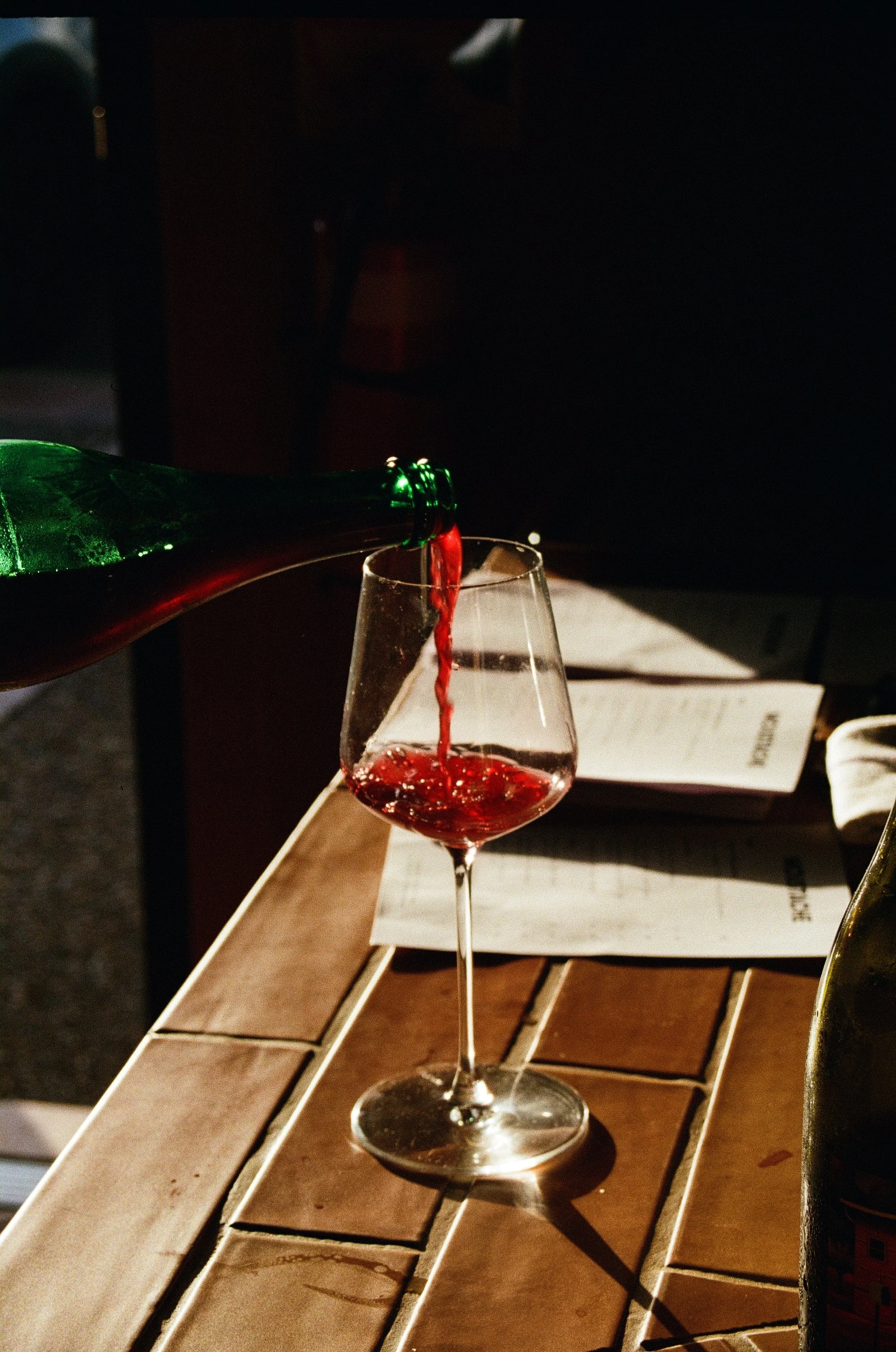 Red wine being poured into a glass on a wooden table with papers underneath. Gold Coast | Byron Bay Food Photography by Joey Bailey