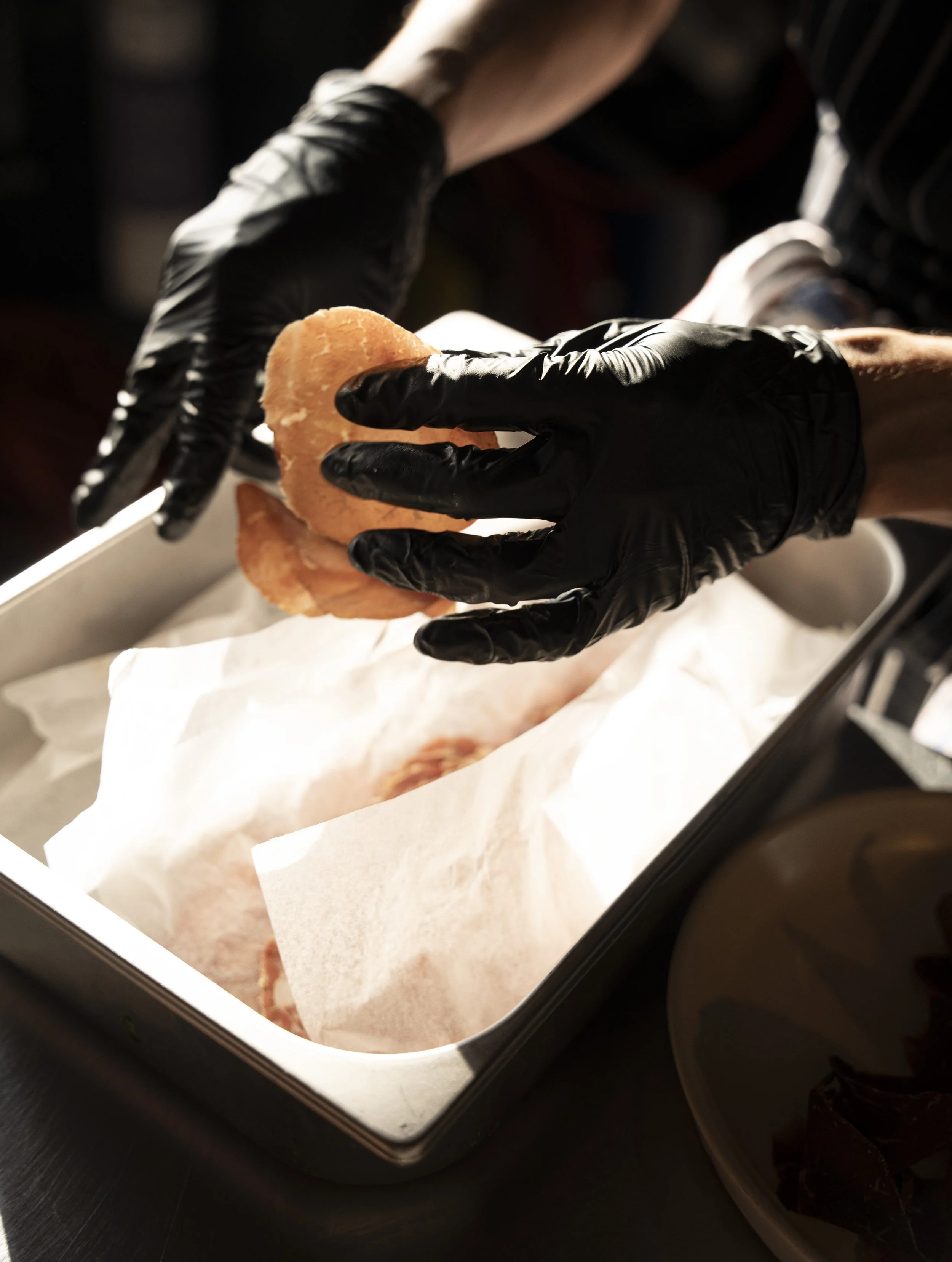 Chef wearing black gloves placing a piece of food into a box lined with white parchment paper. Gold Coast Food Photography by Joey Bailey