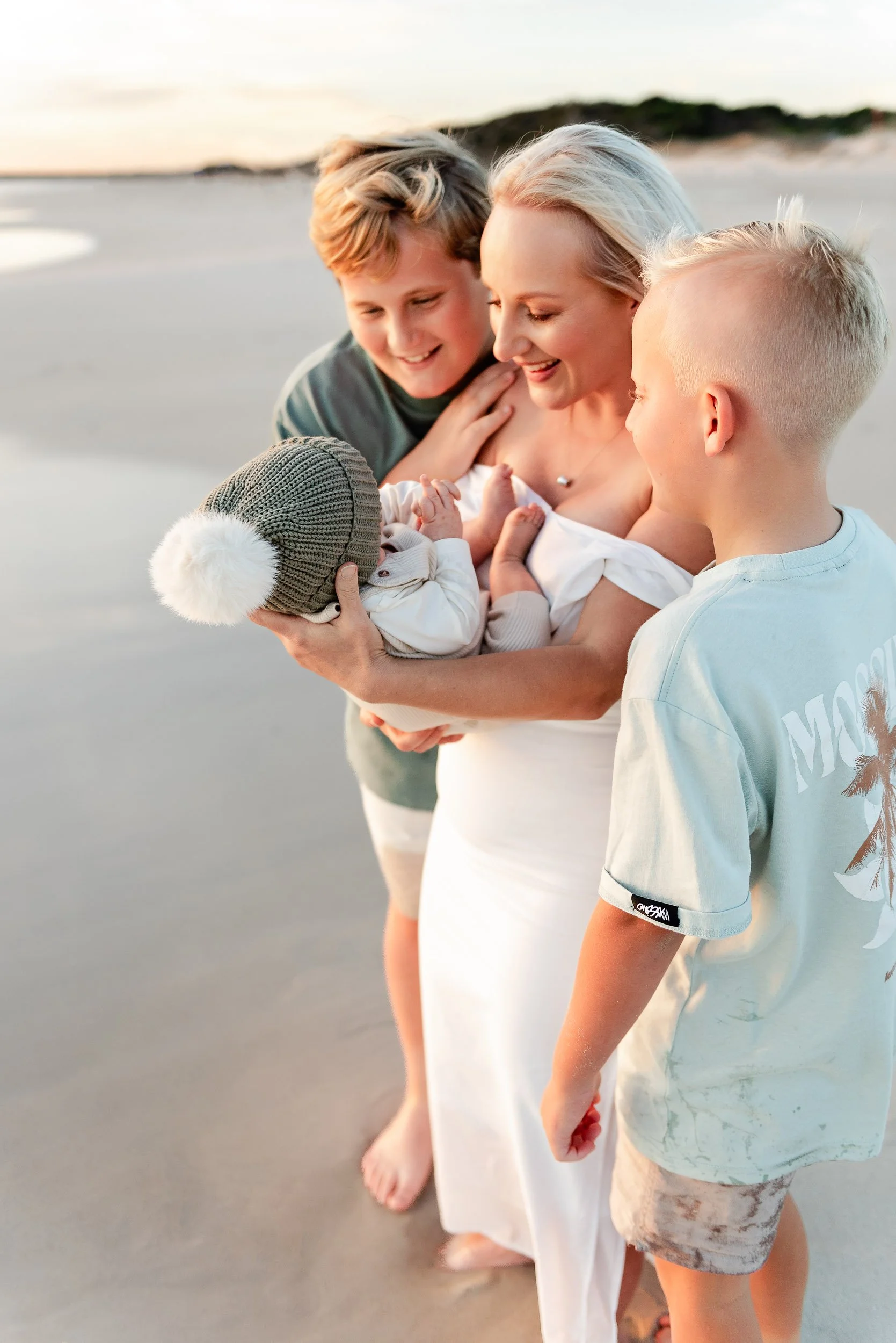 Family on the beach with a baby, mother, and two children enjoying sunset.
