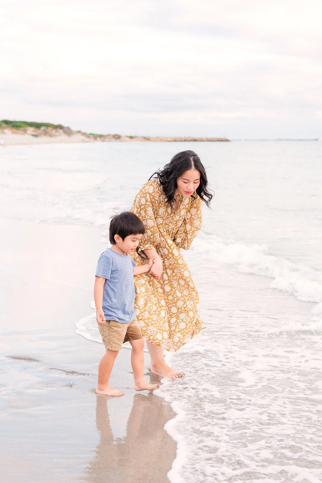A woman and young boy holding hands walking on the beach at the shoreline