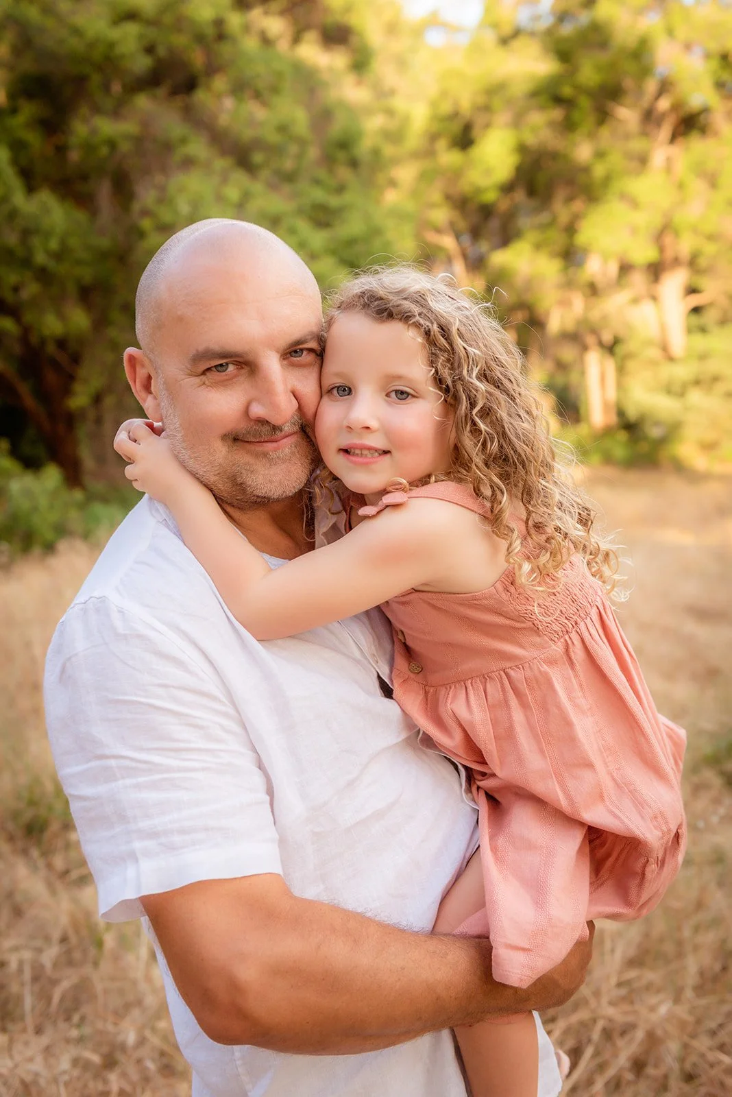 A man holding a young girl in a park with trees in the background.