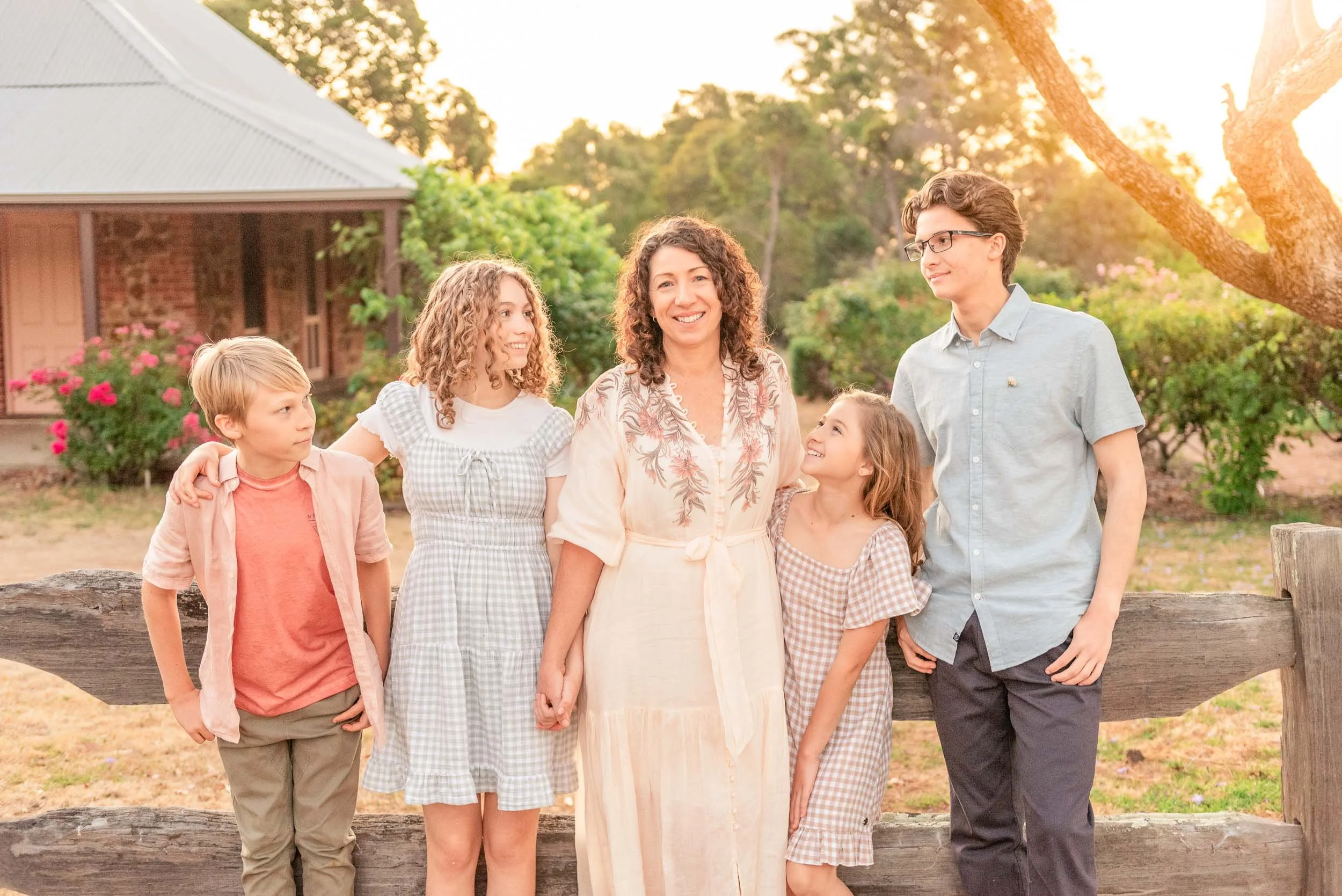 A woman with five children standing outdoors by a wooden fence during sunset.