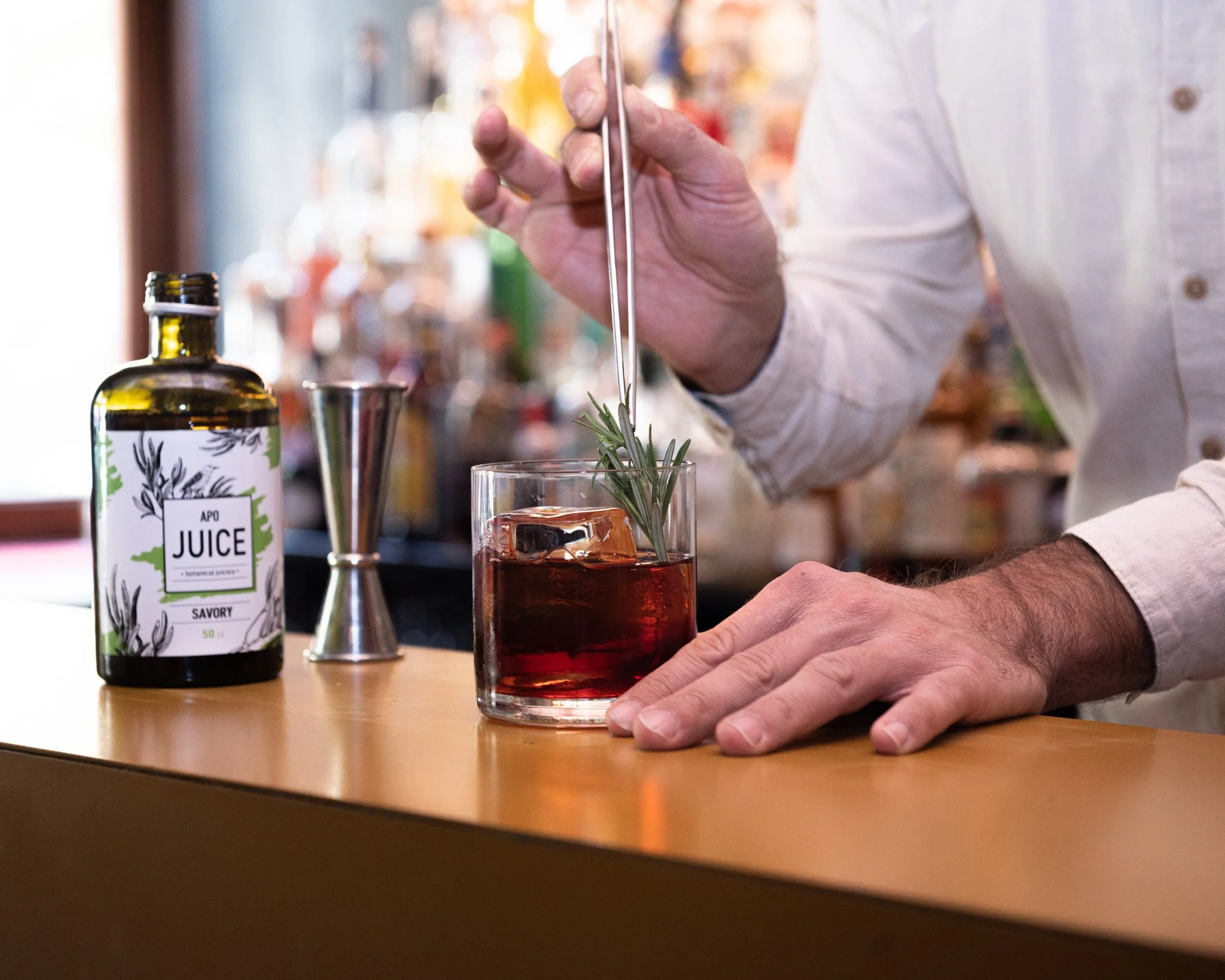 Bartender prepares a non-alcoholic cocktail with a BOTANICA botanical extract, garnishing the drink with rosemary while mixing.