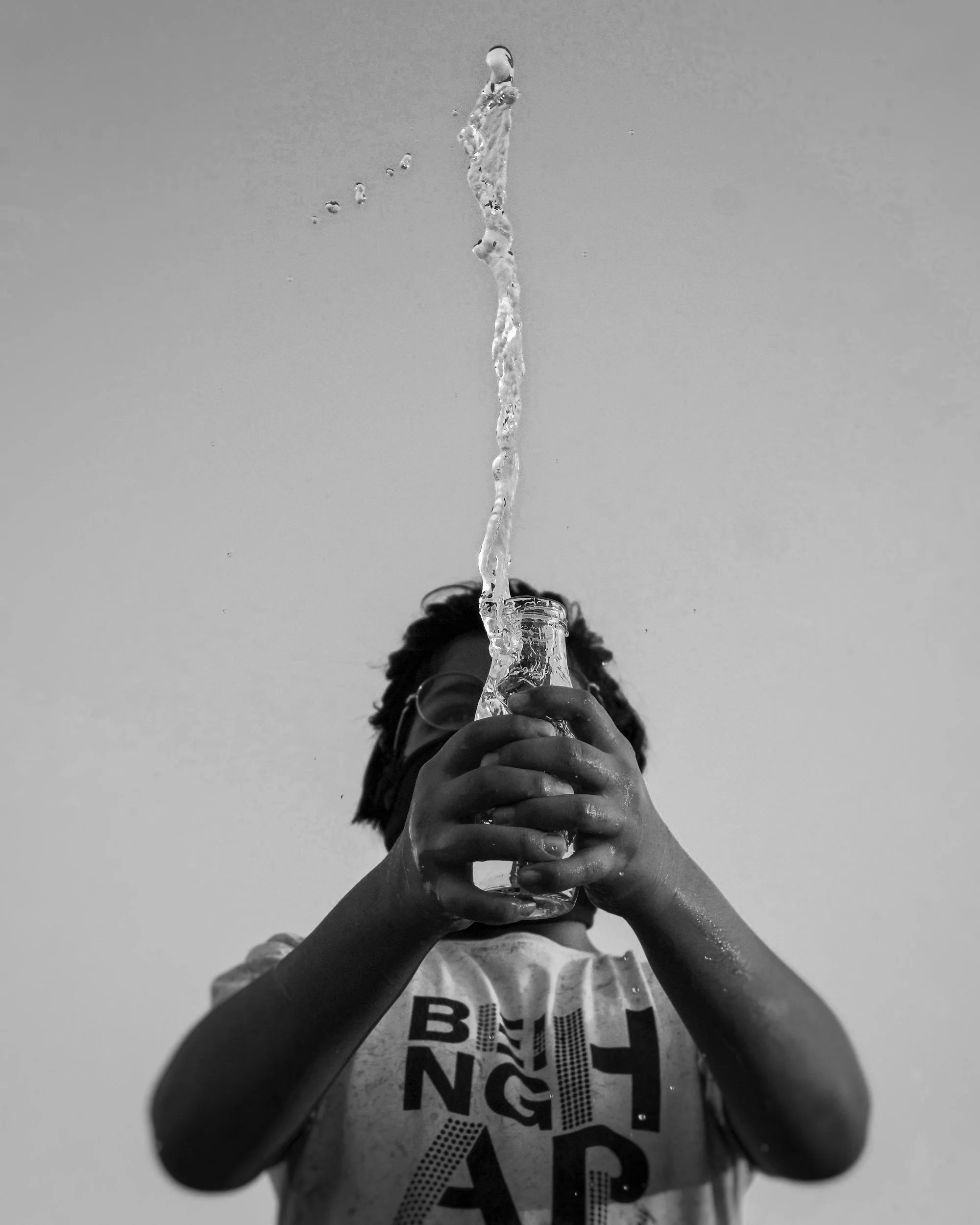 A person holding a glass bottle upside down with water pouring out, captured from below in black and white.