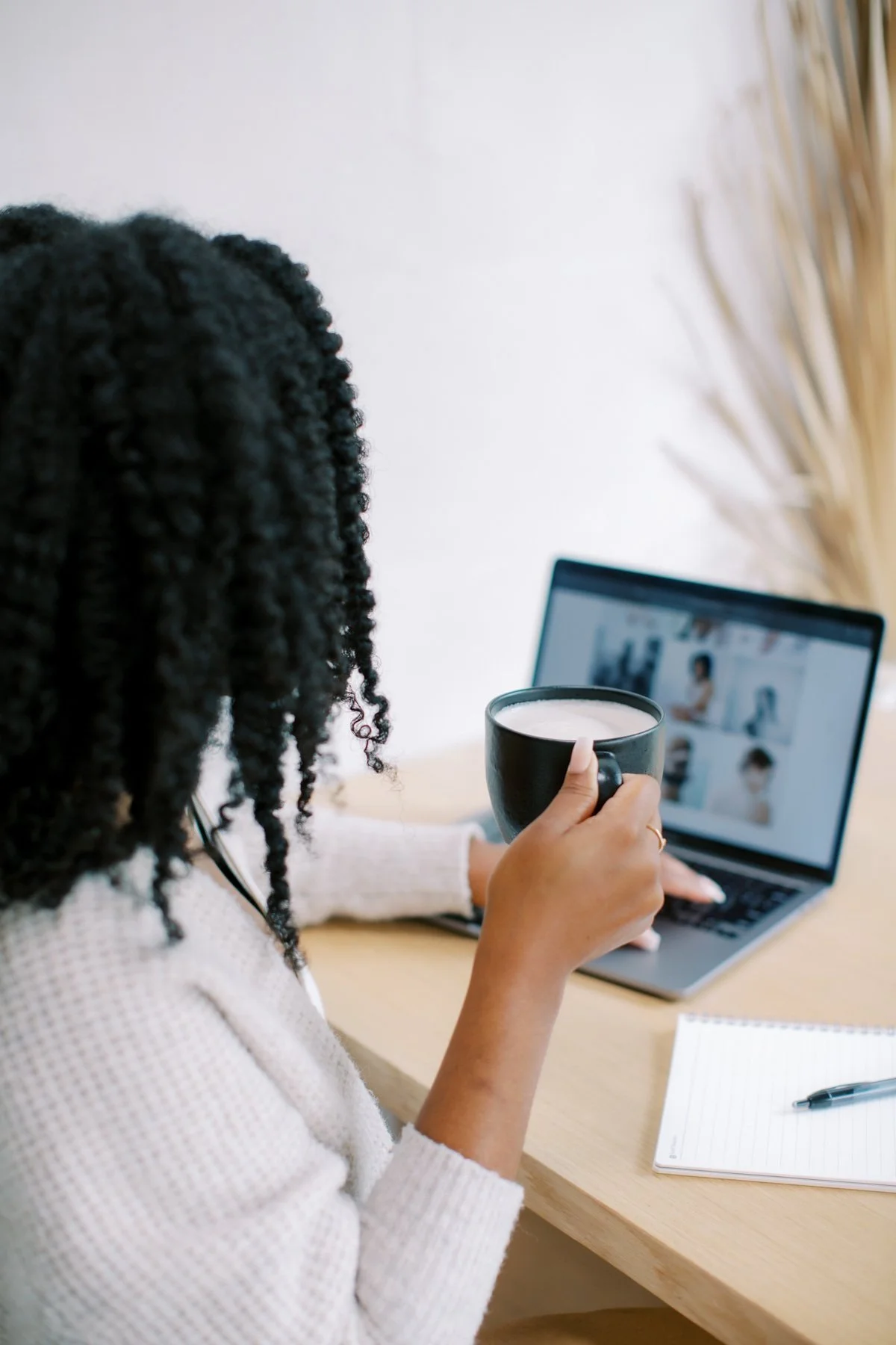 Woman with black hair drinking coffee while at her computer desk.
