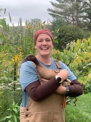 Elle Odyn standing holding a brown duck in her garden wearing overalls and smiling. Elle Odyn teaches SEO Copywriting to neurodivergent business owners in Ottawa and across Canada.