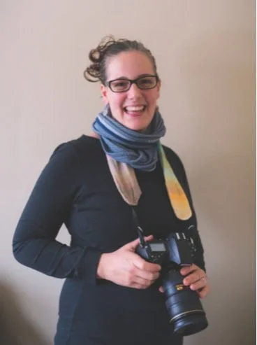 Woman with glasses, colourful scarf on camera and wearing a black dress.