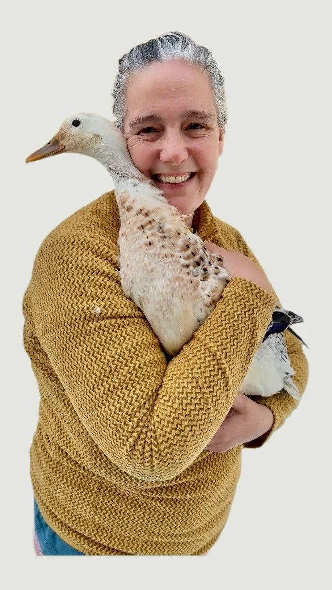 Smiling woman in a yellow patterned sweater holding a duck with a white background.