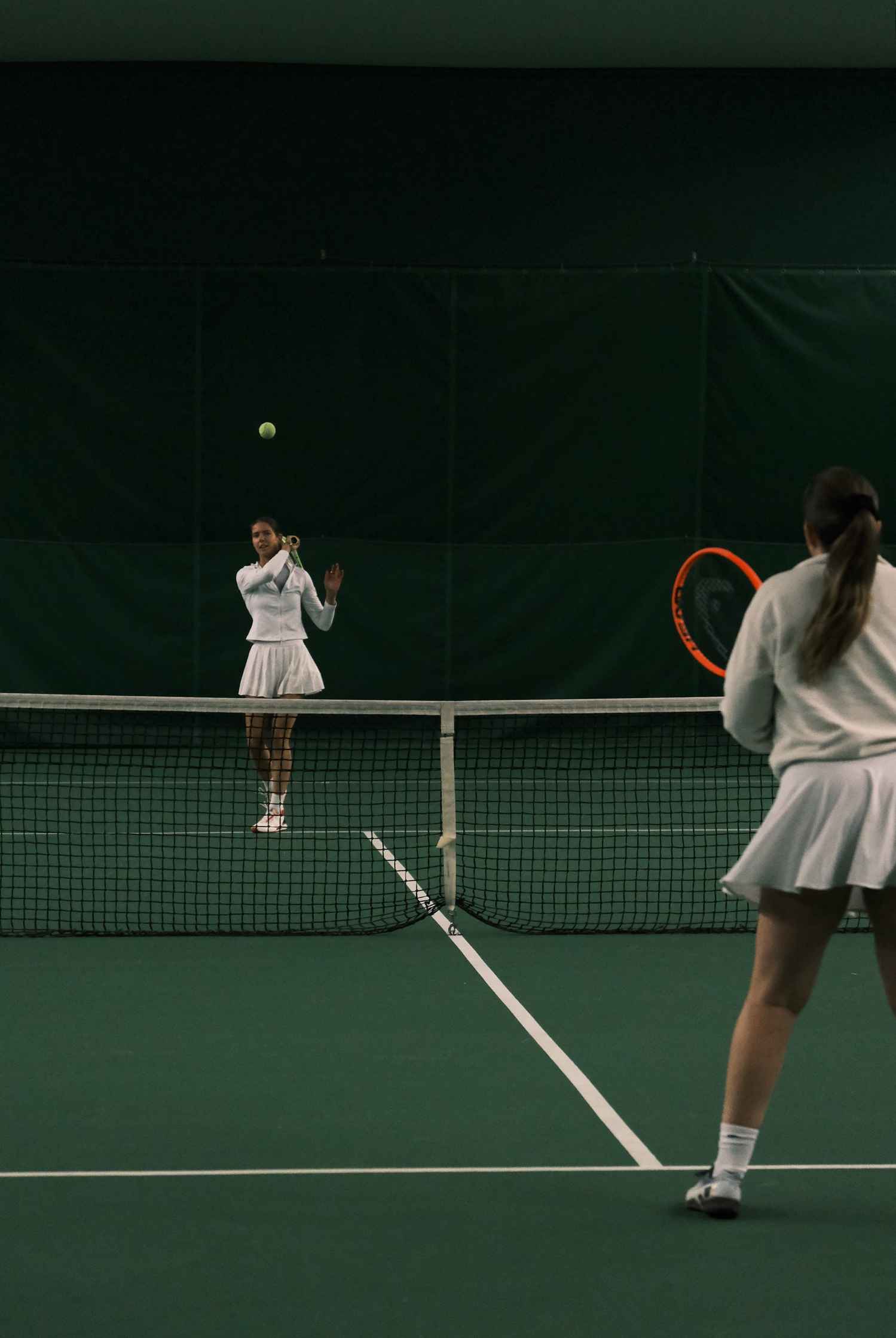 Kaksi naista pelaa tennistä, toinen on juuri lyömässä palloa verkon toisella puolella.