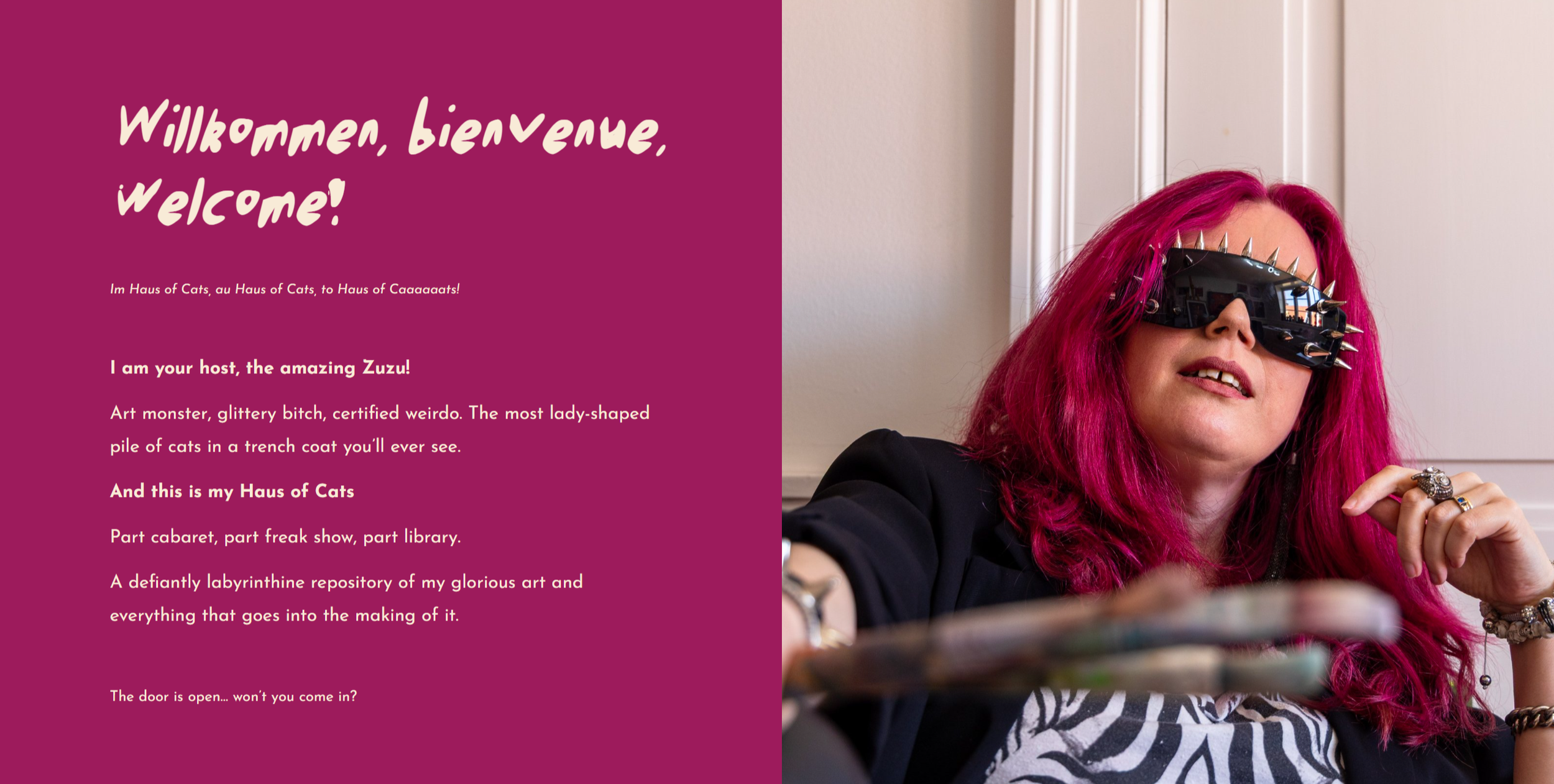 Woman with bright pink hair wearing spiked sunglasses, black blazer, and jewelry, leaning against a wall.