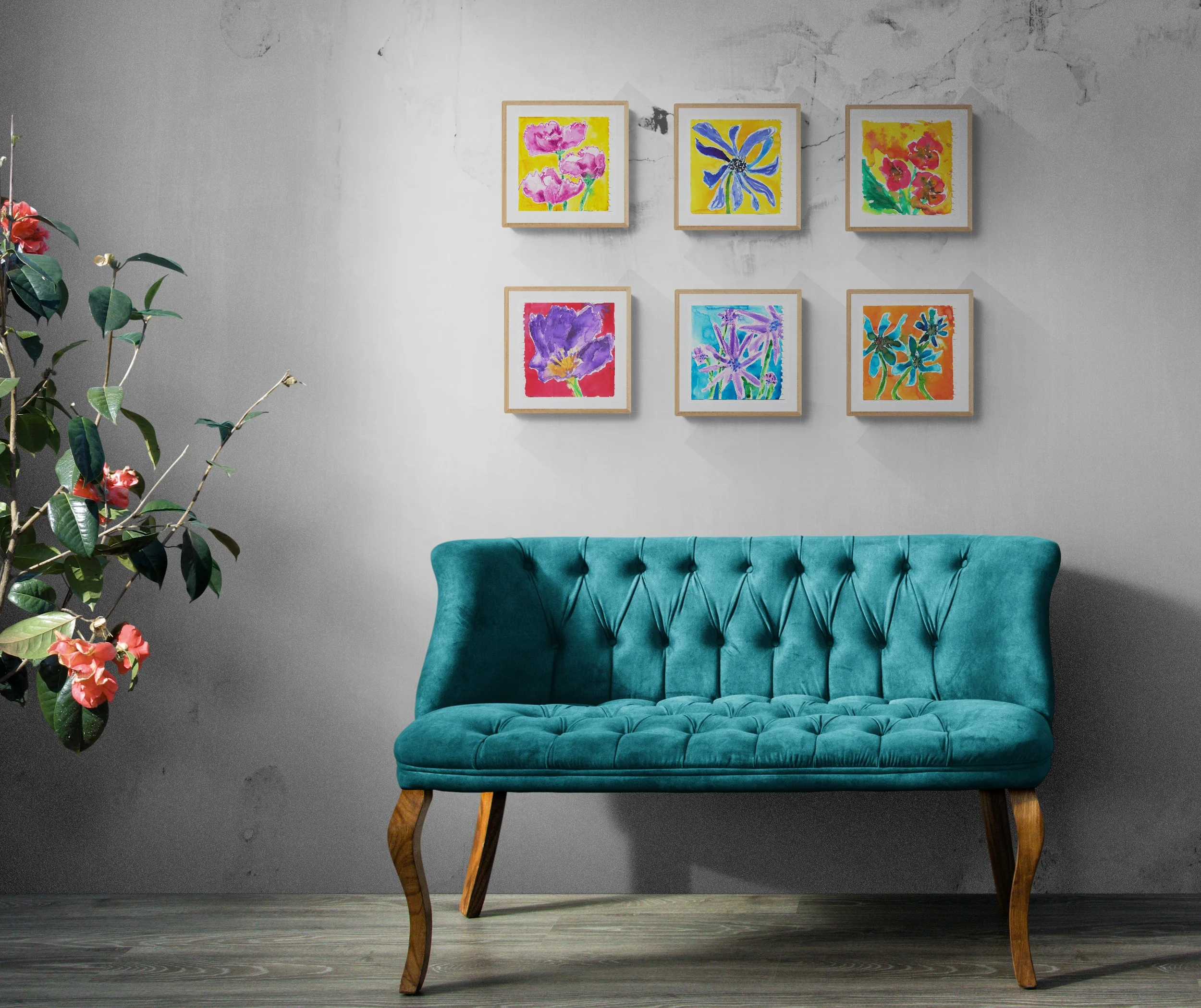A teal velvet tufted sofa with wooden legs, in front of a gray wall with a set of six colorful abstract floral paintings arranged in two rows, and a large potted plant with pink flowers on the left.