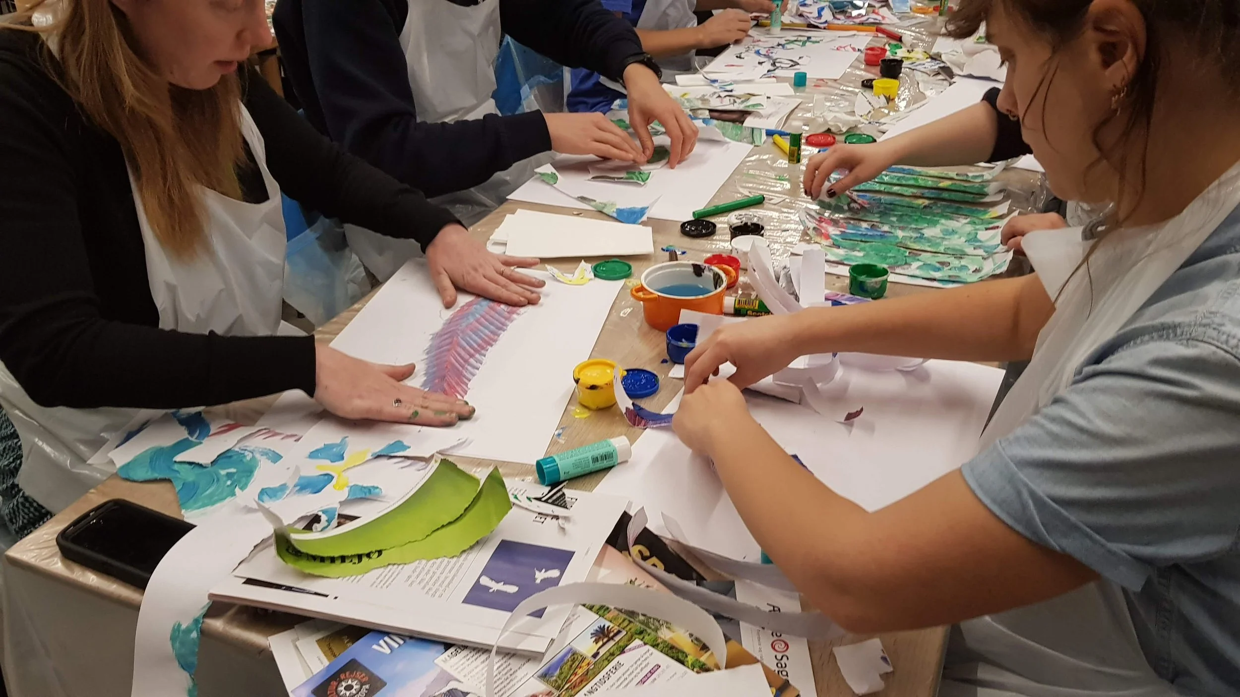 People engaged in a paper painting art project at a table covered with art supplies such as paper, paints, and brushes.
