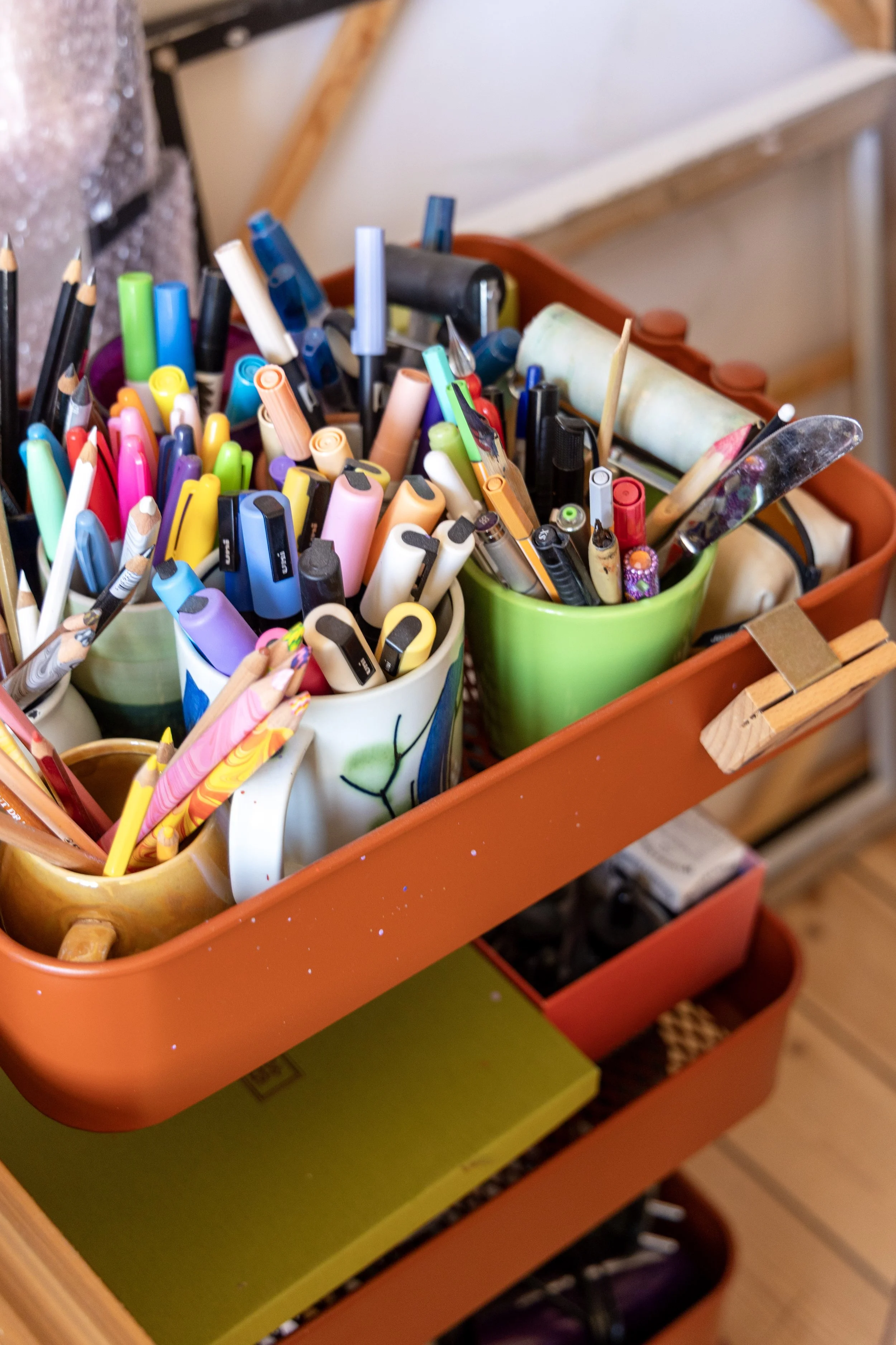 A rolling cart filled with assorted markers, pens, pencils, and art supplies in colorful containers.