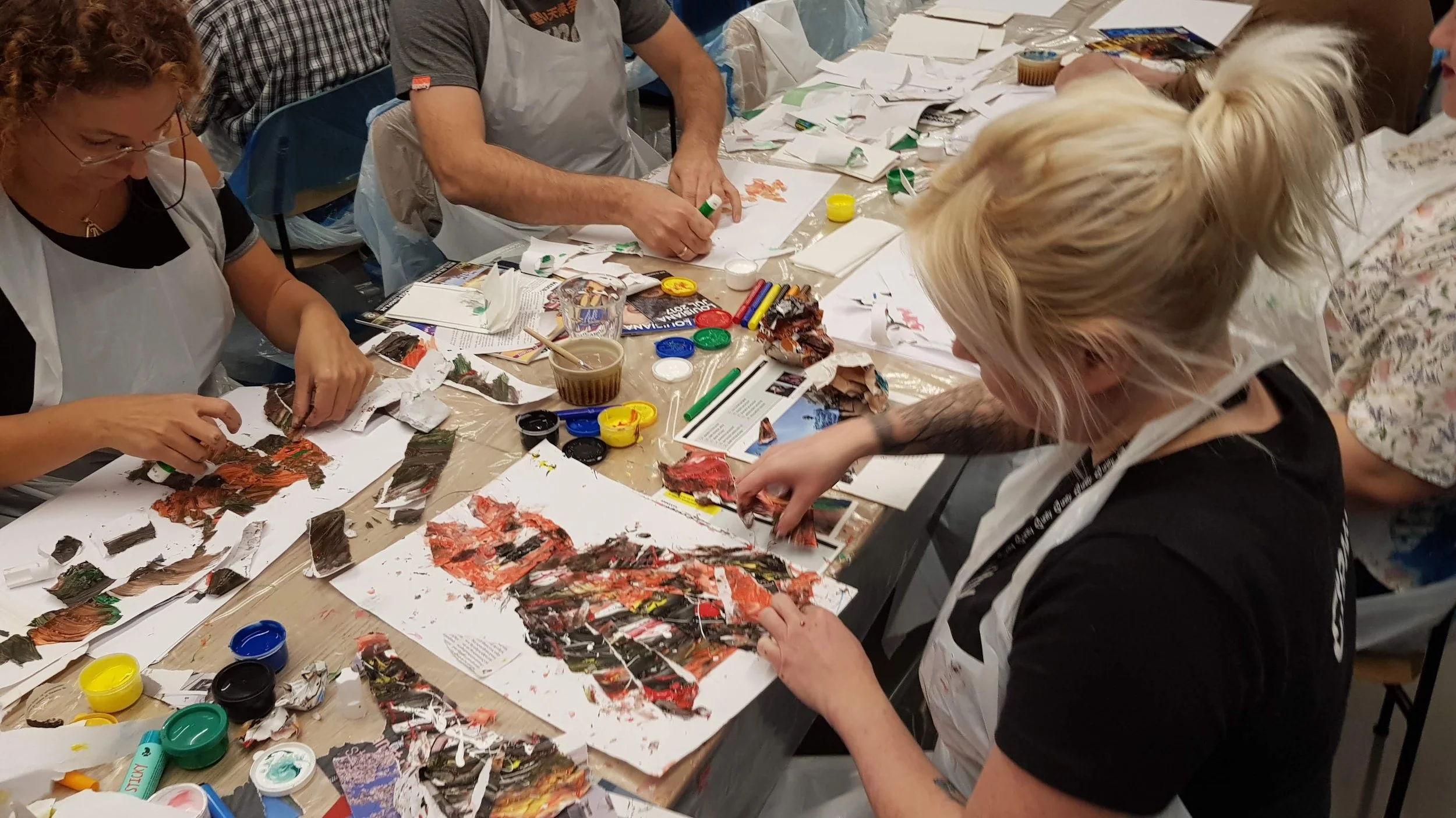 People sitting around a table engaging in an art project, using torn paper and paint with various art supplies scattered on the table.