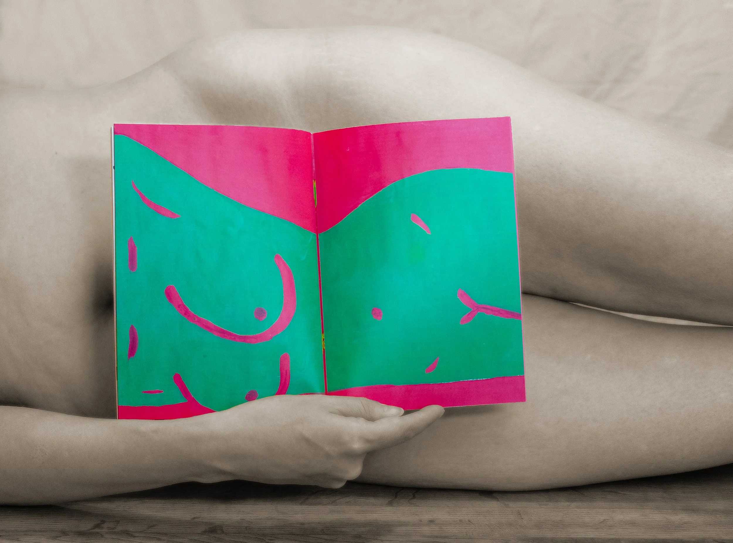 Close-up of a person holding an abstract, colorful zine open, displayed against a soft, neutral background.