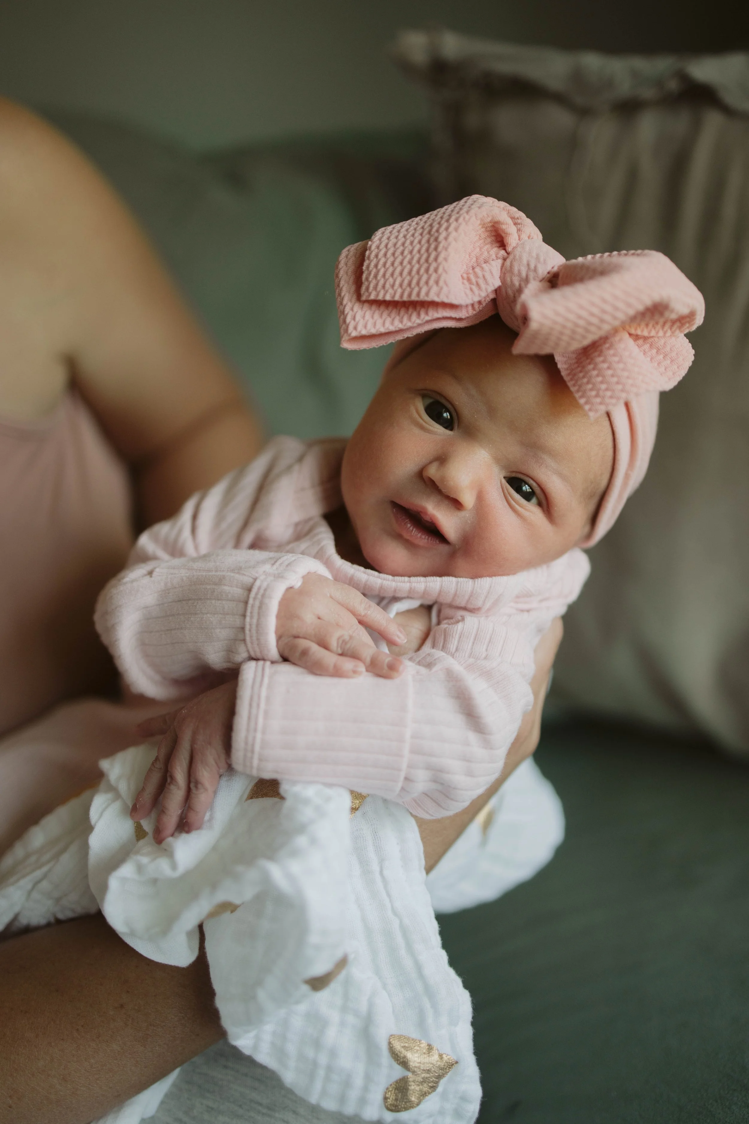 Babygirl in mom's arms smiling at the camera with a pink bow
