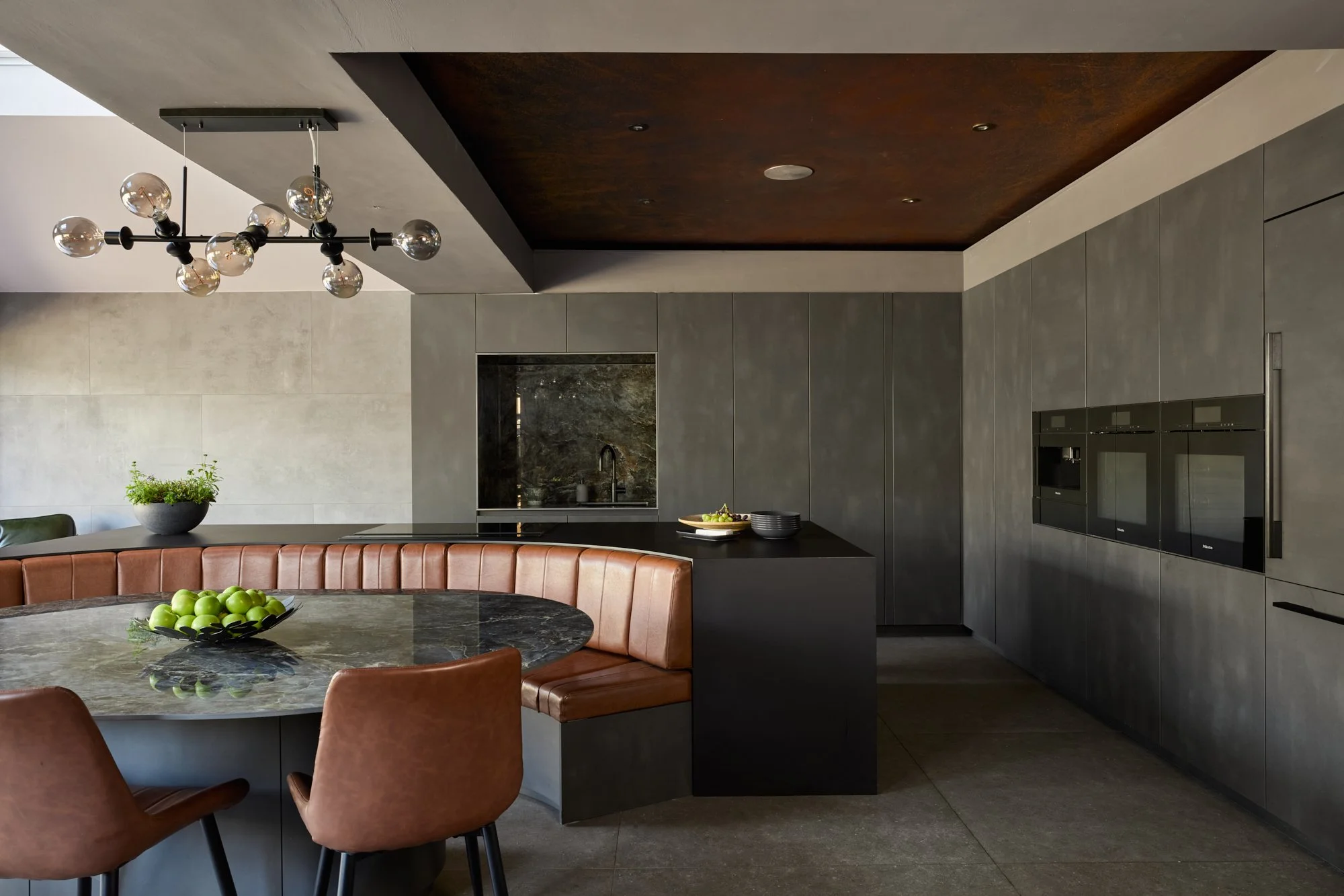 A striking combination of moody dark cabinetry and burnt orange seating combine for a dramatic space in this beautiful kitchen. 

Kitchen design: @ashley_halcyon
Custom-made banquette: @simpson.york.limited
Stone: @crlstone in Labradorite Royal Blue
