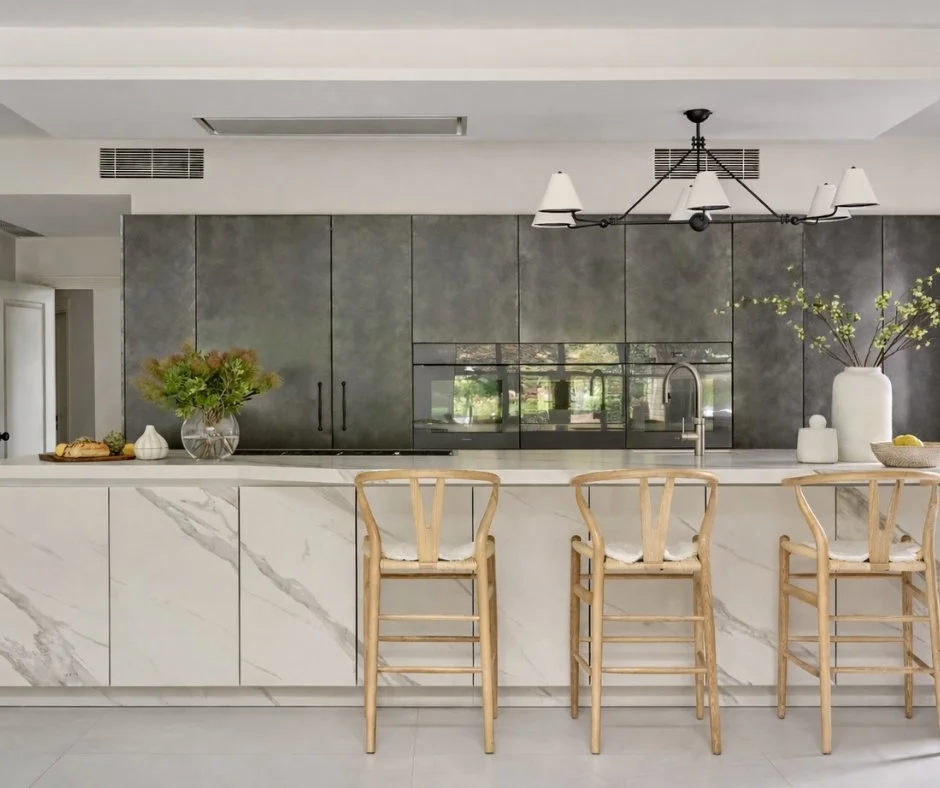 Mixing materials creates an eye-pleasing contrast in this elegant kitchen. 

The soft marbling on the island provides a calming complement to the depth of the textured cabinetry behind. The warmth of the light timber chairs ties the look together to 
