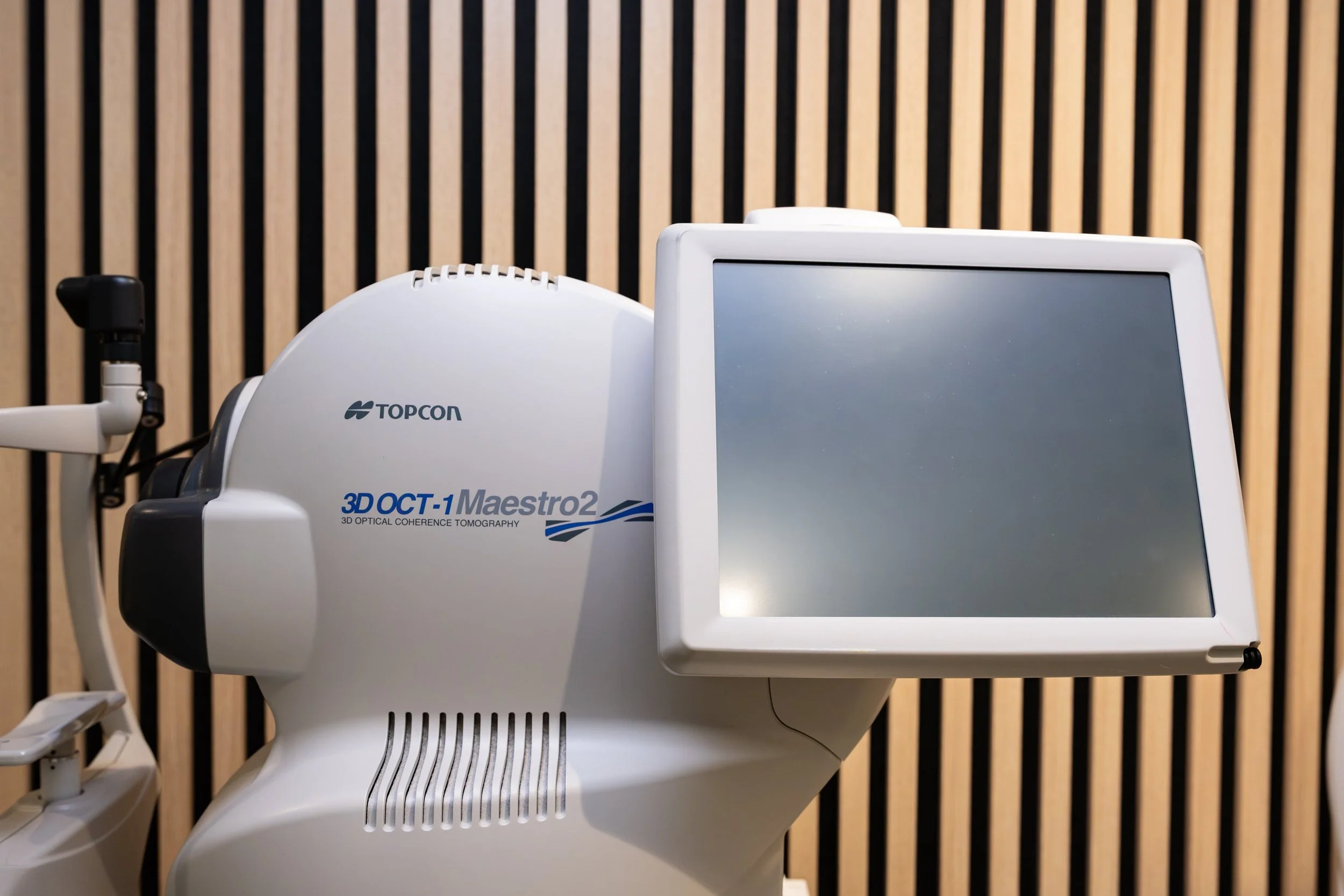 Medical imaging device with a digital screen, labeled 'TOPCON 3D OCT-1 Maestro2' on a wooden panel background.