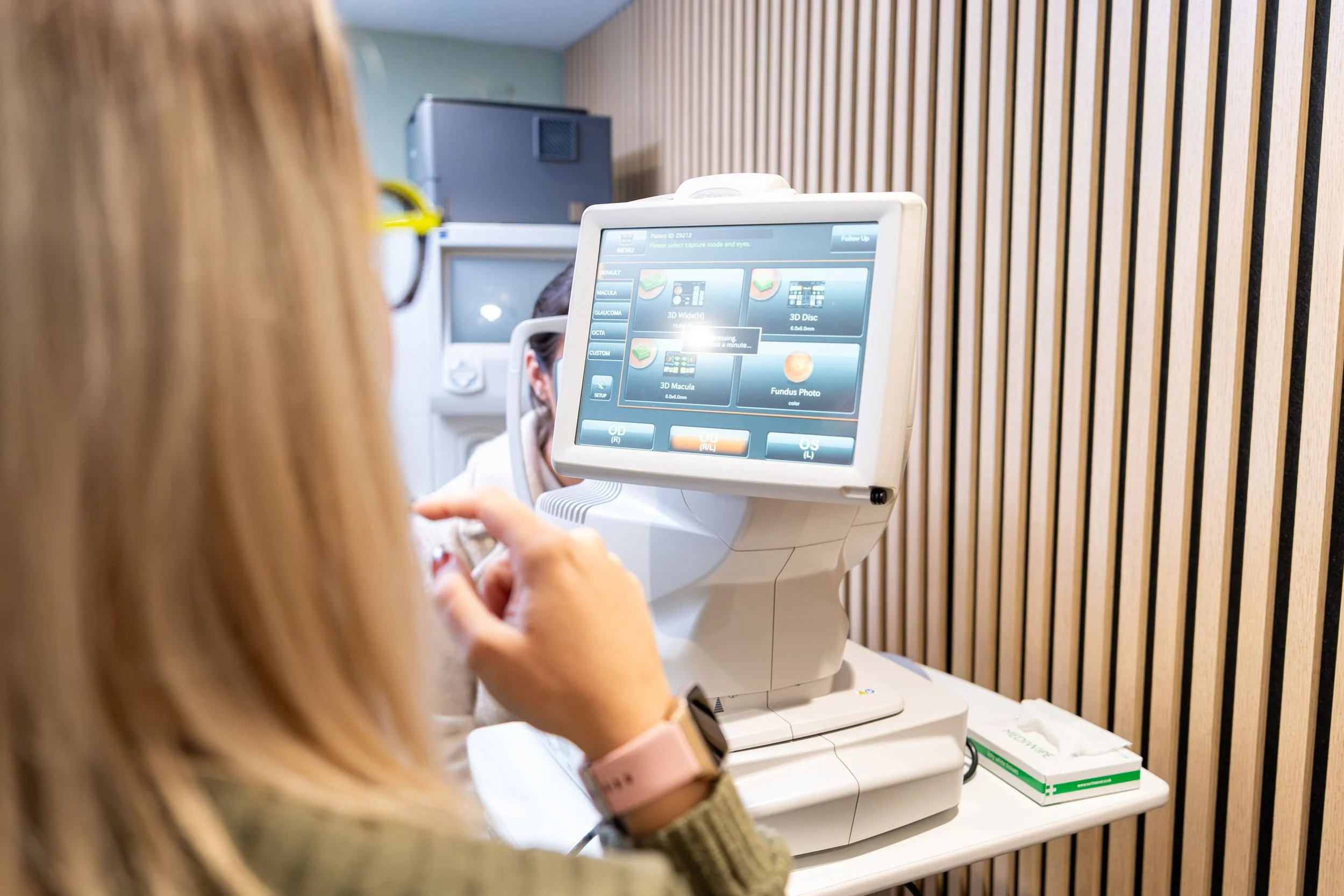 A woman undergoing an eye exam using a non-contact autorefractor at an eye care clinic.