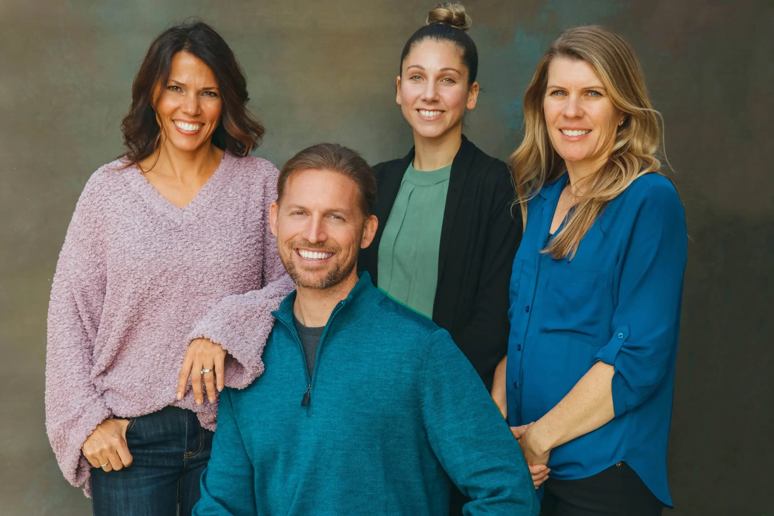 Four adults, three women and one man, smiling together as a functional medicine team in front of a neutral studio backdrop.