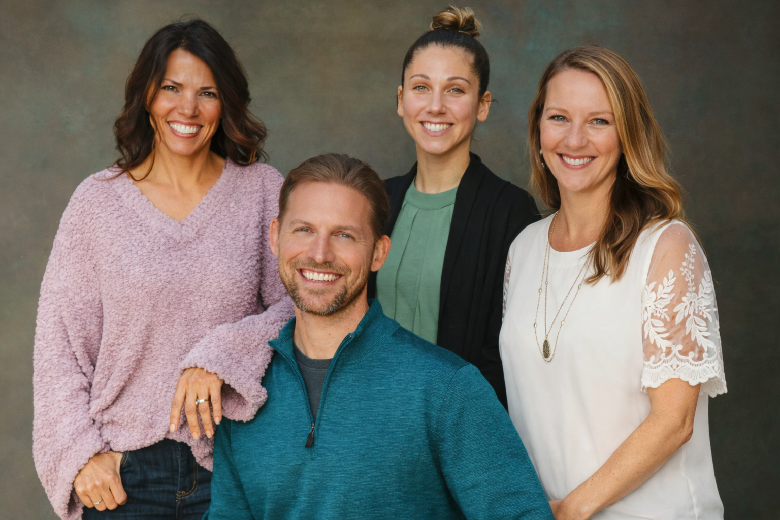 A group of five smiling adults posing together against a neutral background, with three women and one man visibly in the photo.